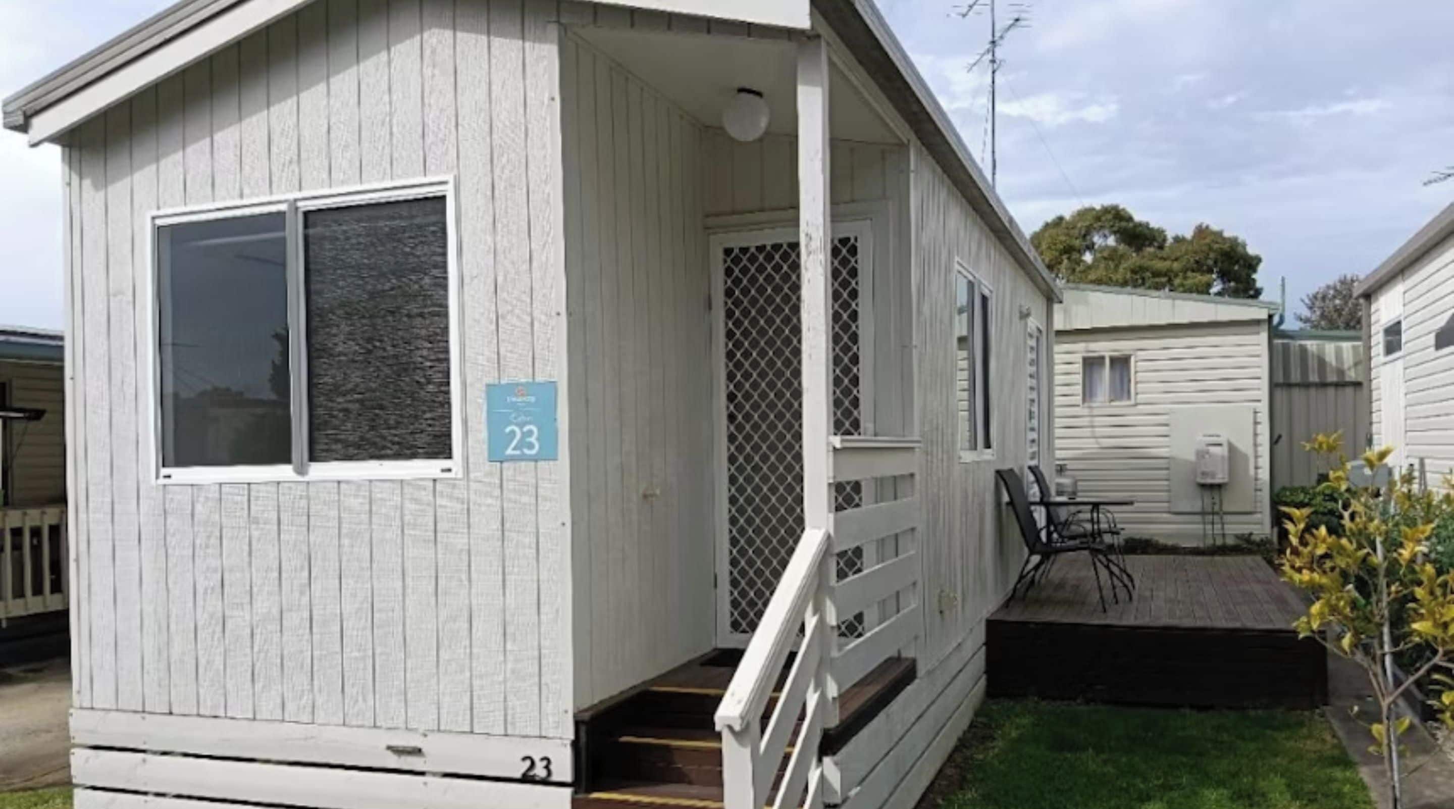 A single-story mobile home with a porch and a small deck, number 23, in a residential area.