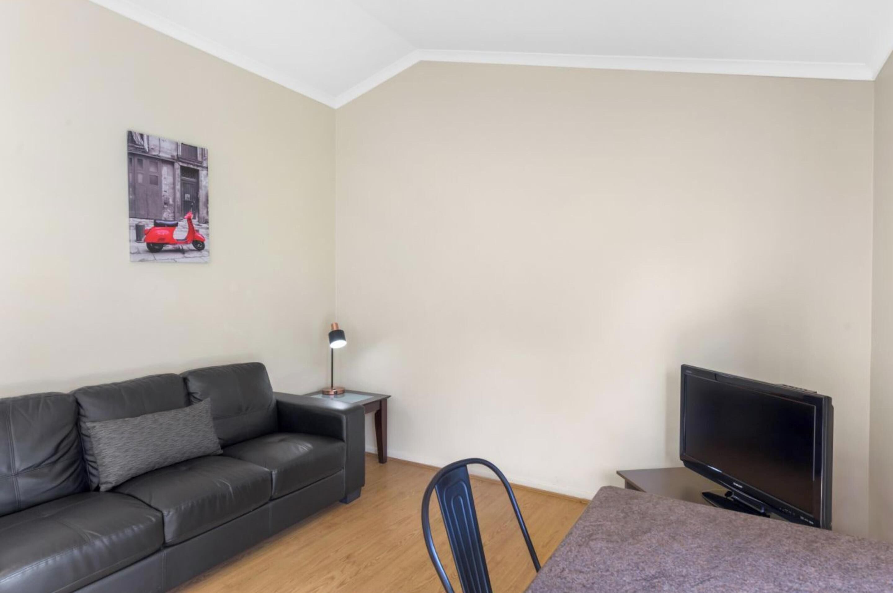 A small, furnished room with a sofa, a chair, a TV, a lamp, and a painting on the wall.