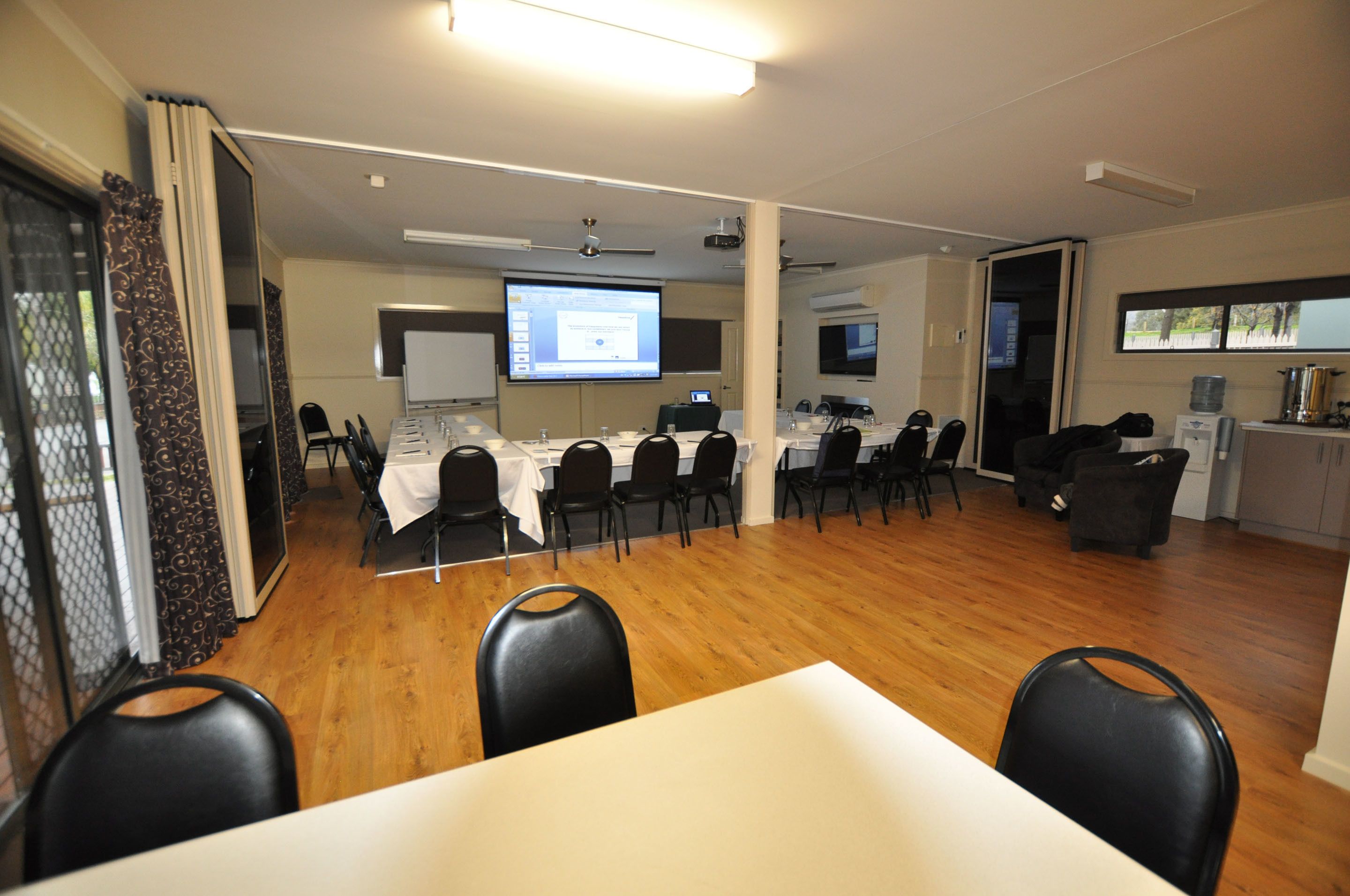 Uma sala de conferência com uma mesa comprida, várias cadeiras, uma tela de projetor e um quadro branco.