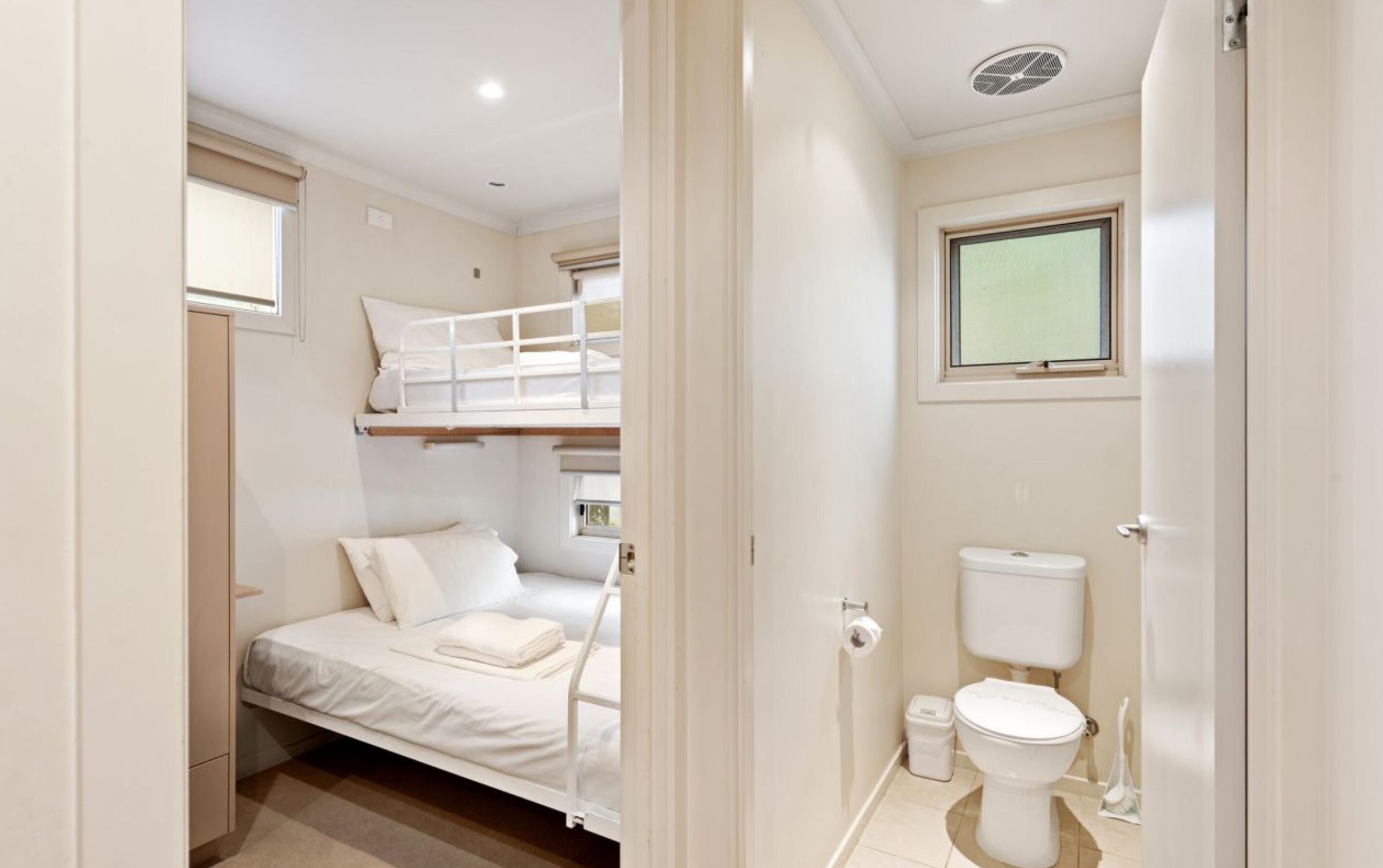 Une chambre à coucher de taille réduite, avec un lit superposé et un lit simple, une petite fenêtre et des toilettes.