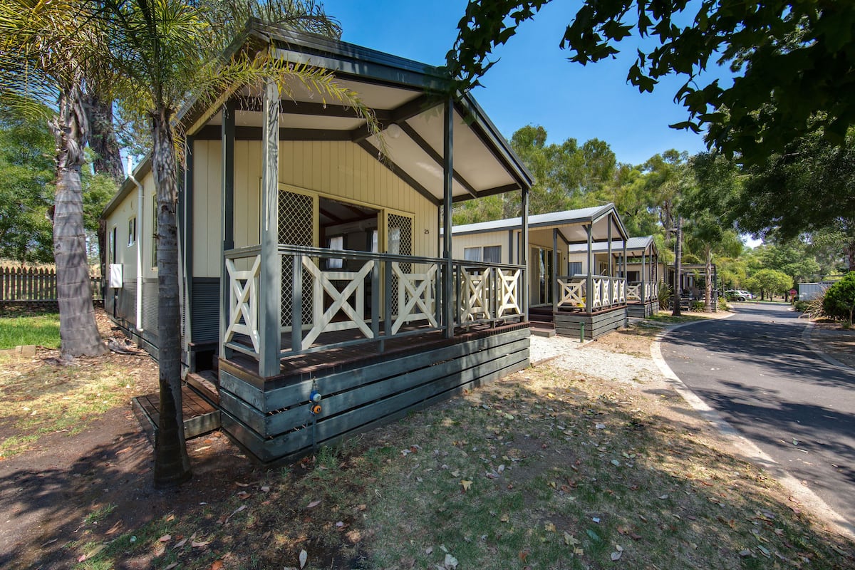 A small, single-story mobile home with a porch and a fenced yard.