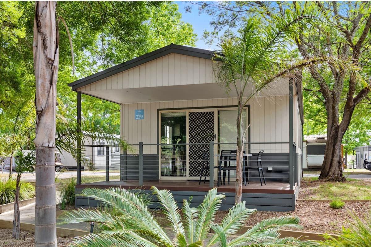 A small, single-story building with a covered porch, numbered 229, surrounded by trees and greenery.