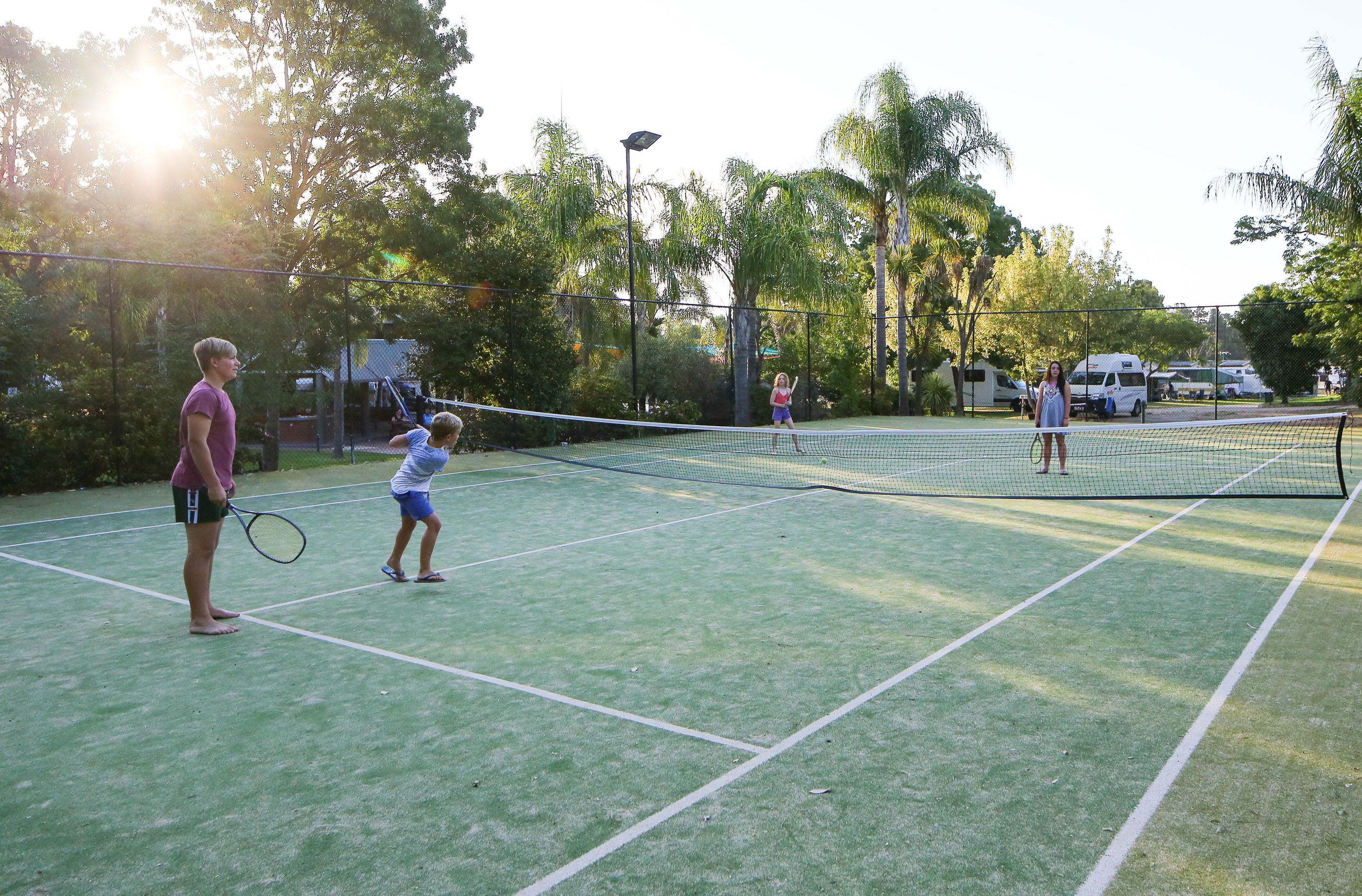 A tennis court with a net, surrounded by trees and a fence.