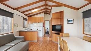 Interior compacto de una autocaravana con cocina americana, un sofá, una mesa de comedor y un televisor.