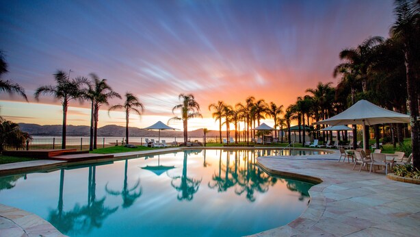 Un área de piscina tranquila con vistas al atardecer, palmeras y sillas de descanso.