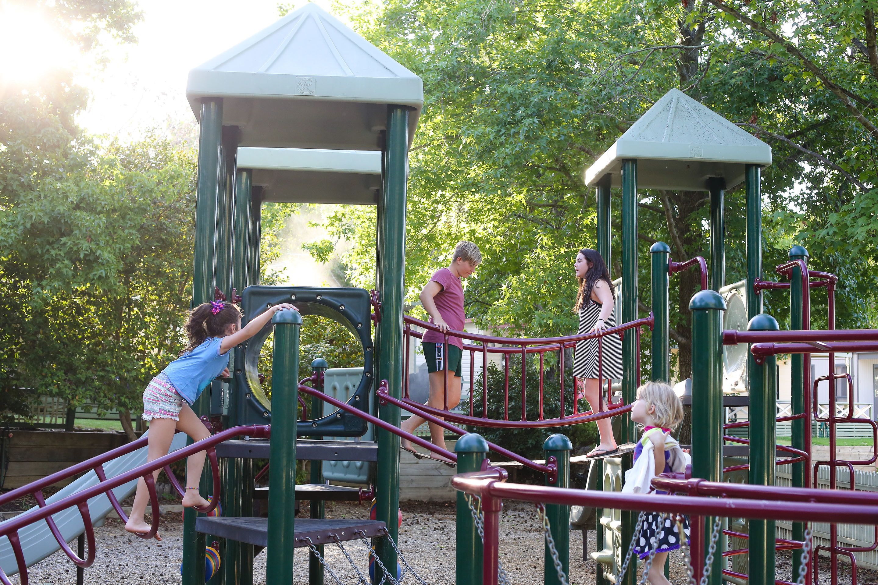 Un parque infantil con varias estructuras de juego, incluyendo un tobogán y zonas de escalada, rodeado de árboles.