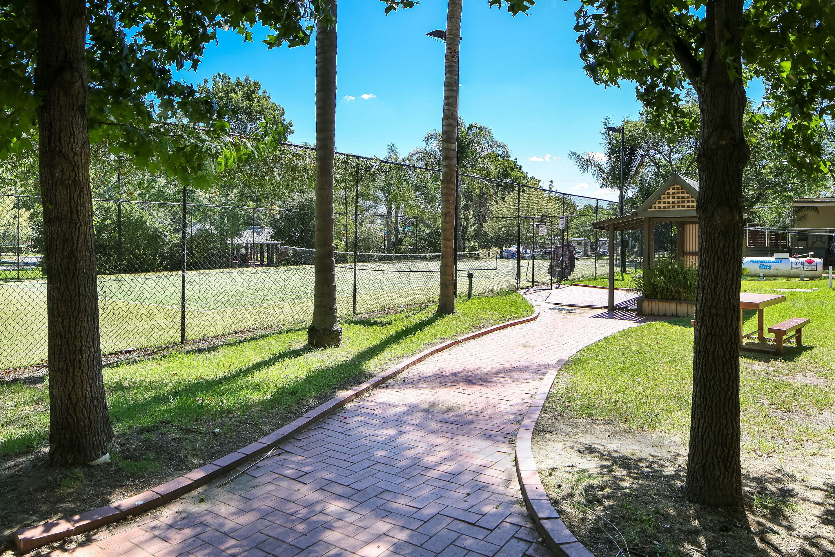 A paved pathway in a park with a fenced area, trees, and a gazebo.