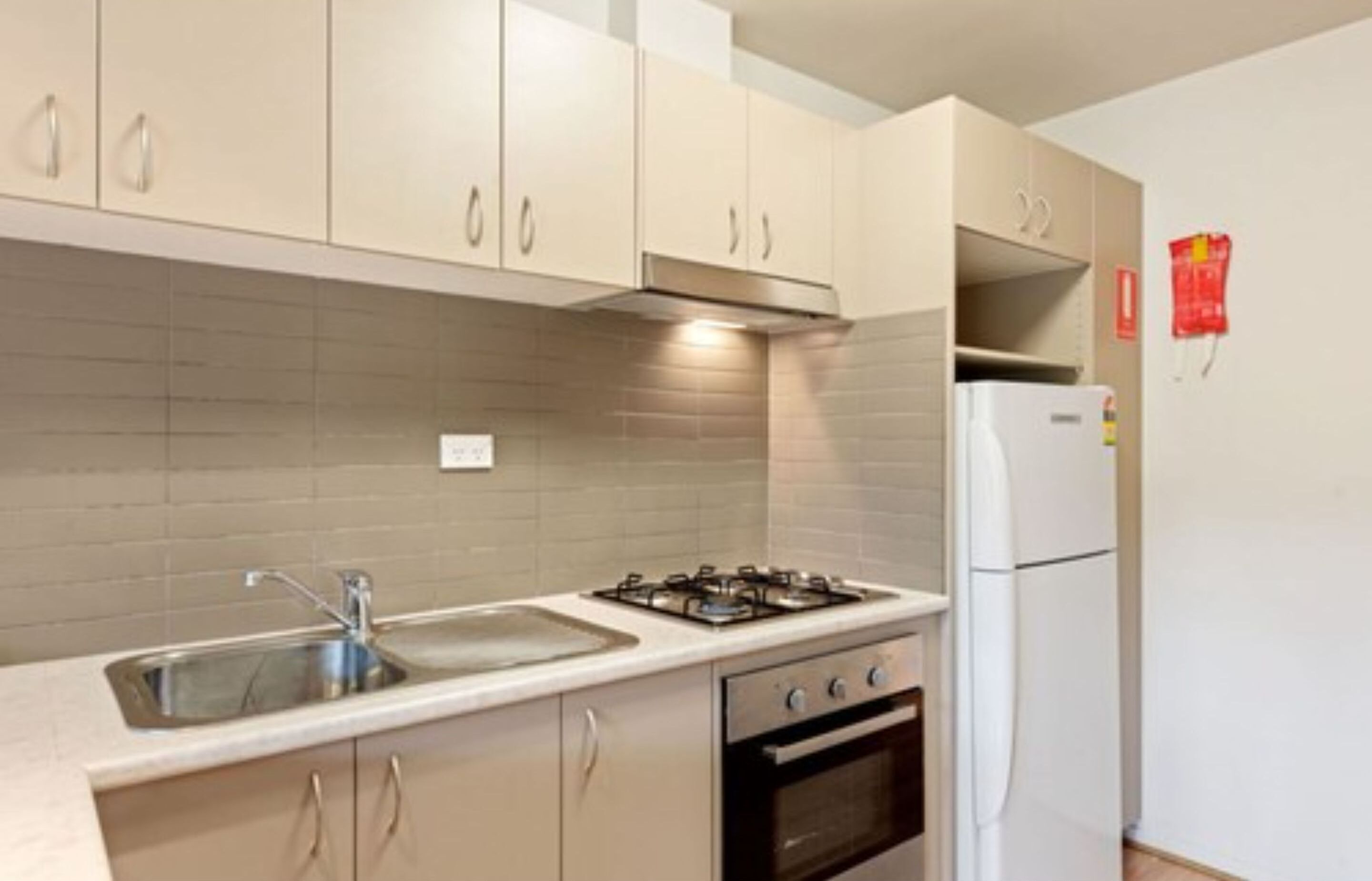 A kitchen with beige cabinets, a gas stove, a sink, and a white refrigerator.