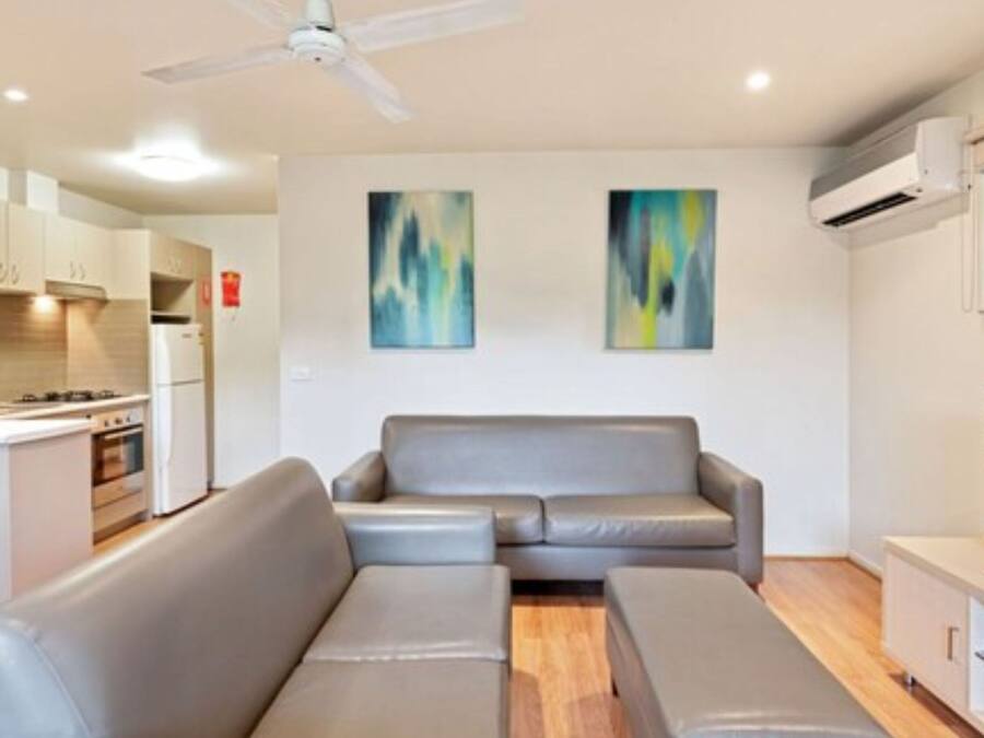 A modern living room with a grey sofa, a television, and a kitchen area in the background.