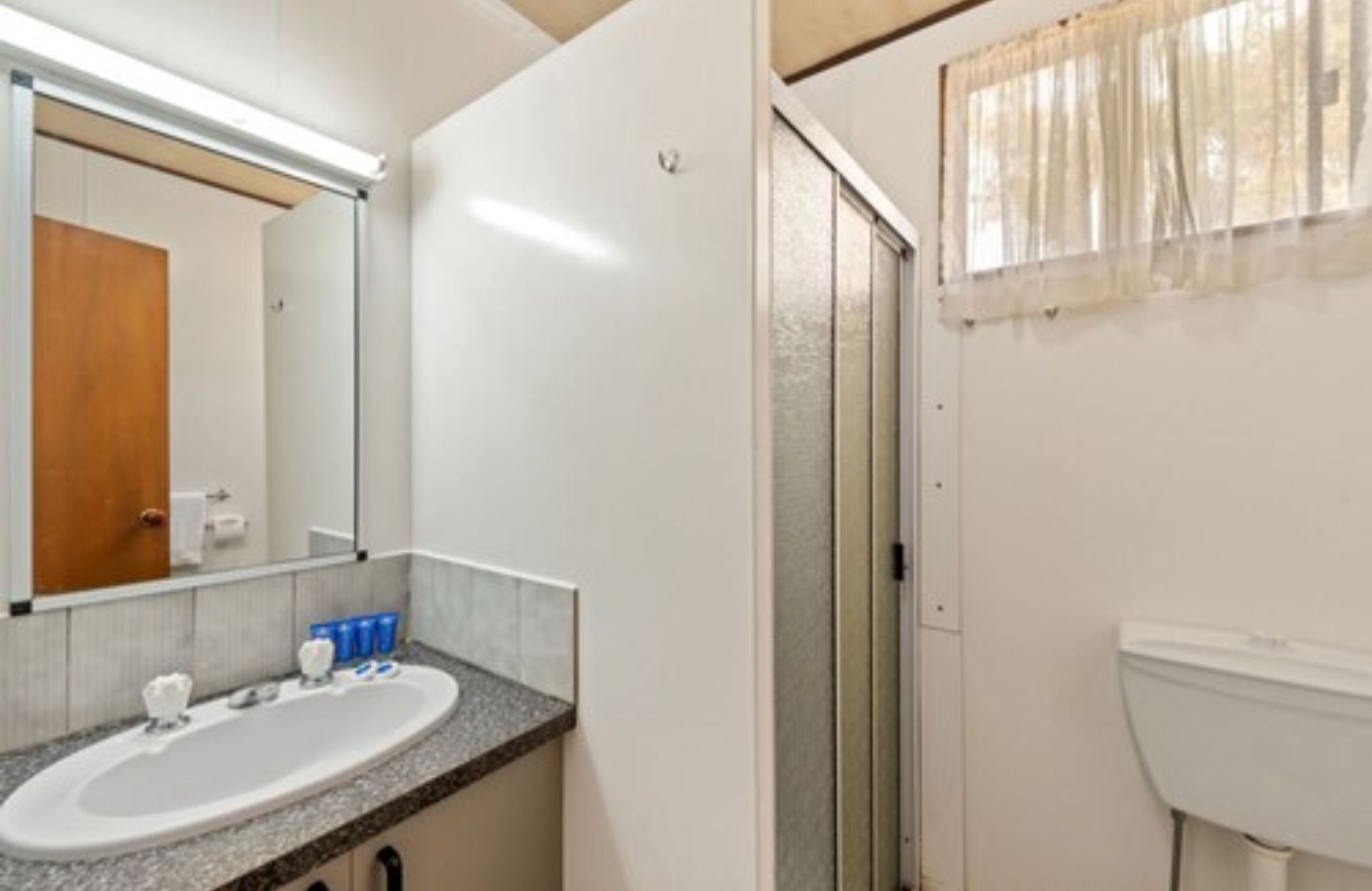Uma casa de banho com lavatório branco, espelho e sanita.