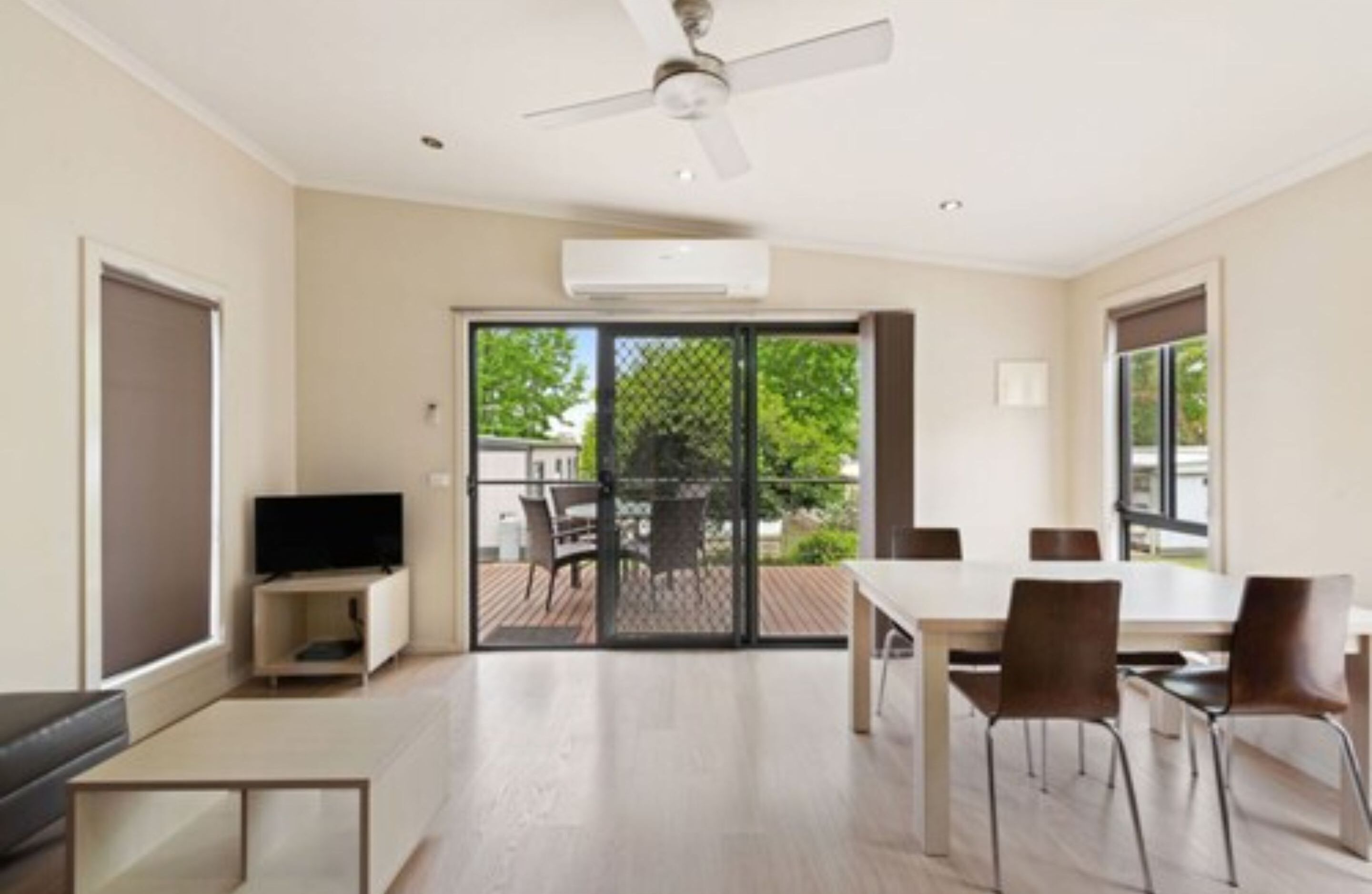 A spacious room with a ceiling fan, a flat-screen TV, a dining table with chairs, and a sliding glass door leading to an outdoor patio.