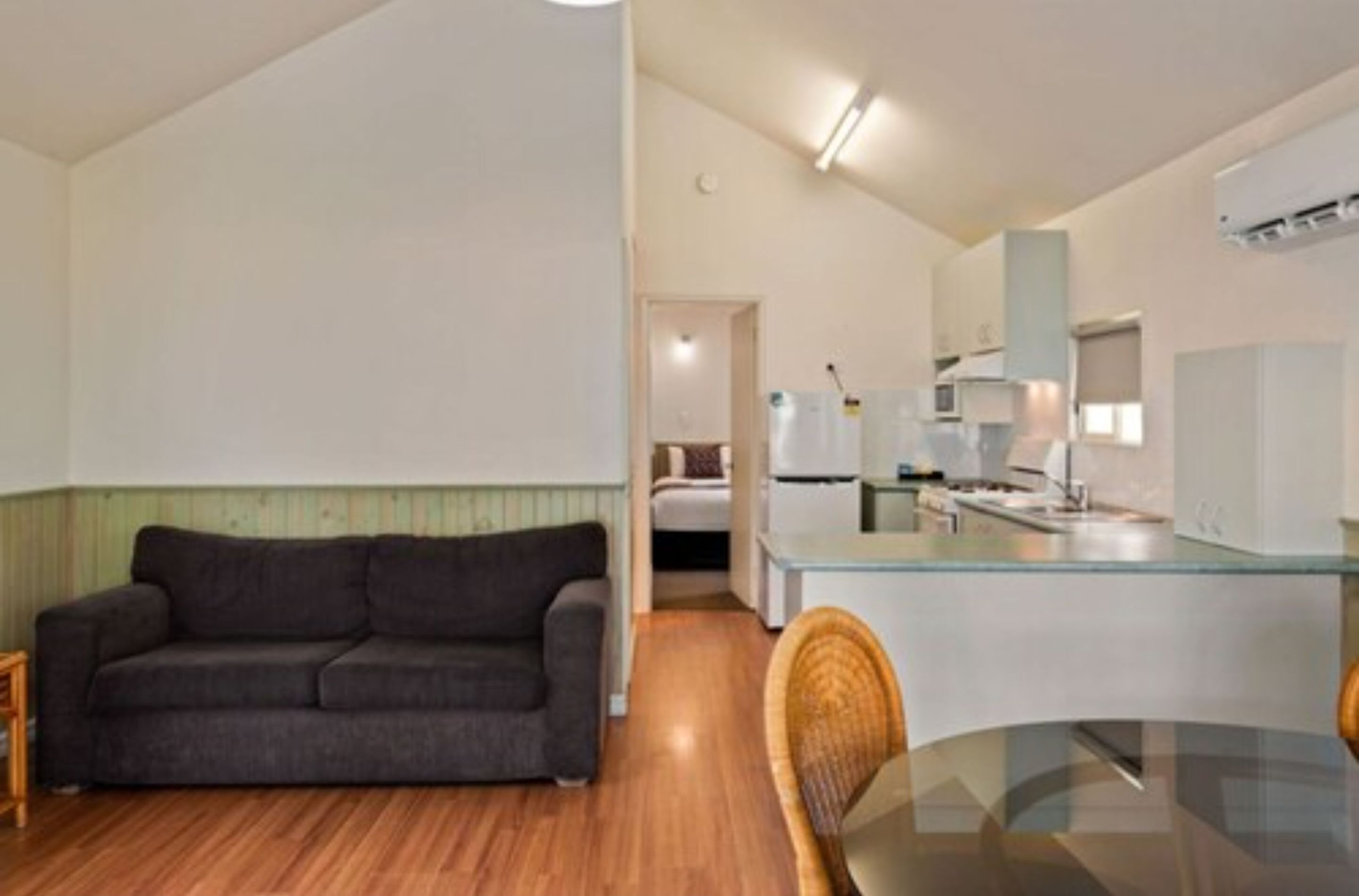 A compact living space with a sofa, a glass dining table, and a kitchenette.