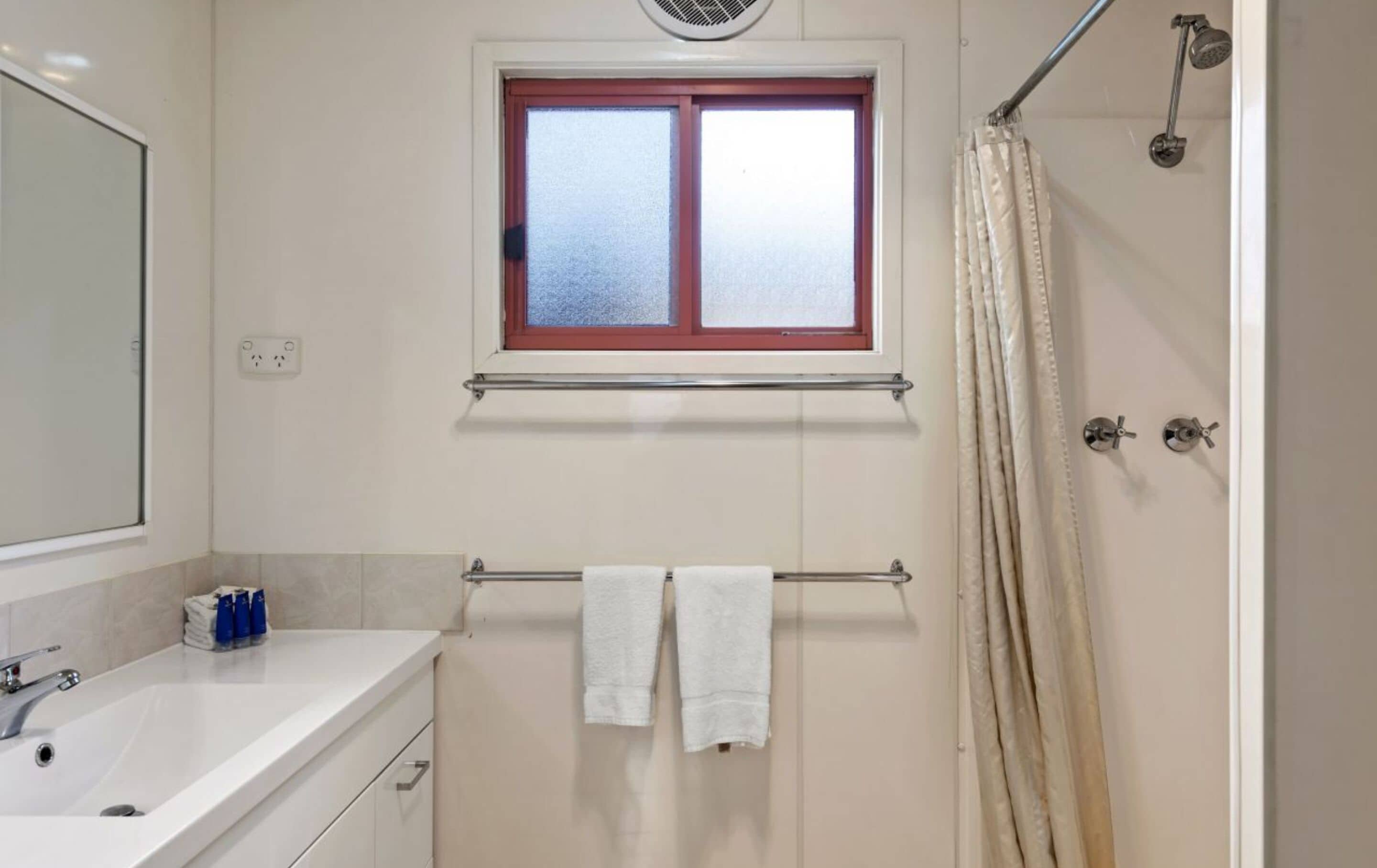 Un baño con ventana, ducha, lavabo y toallas.