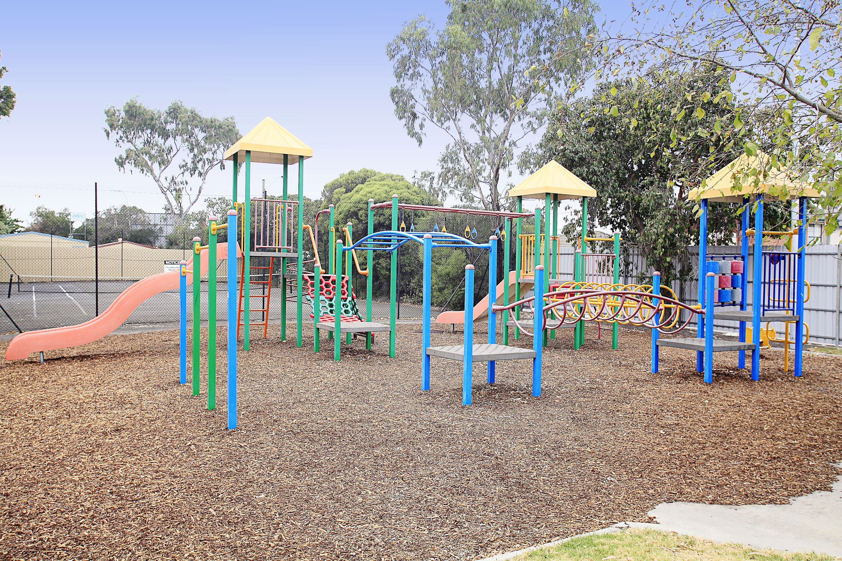 Un parque infantil con diversas estructuras de juego, como toboganes y zonas de escalada, rodeado por una valla y árboles.