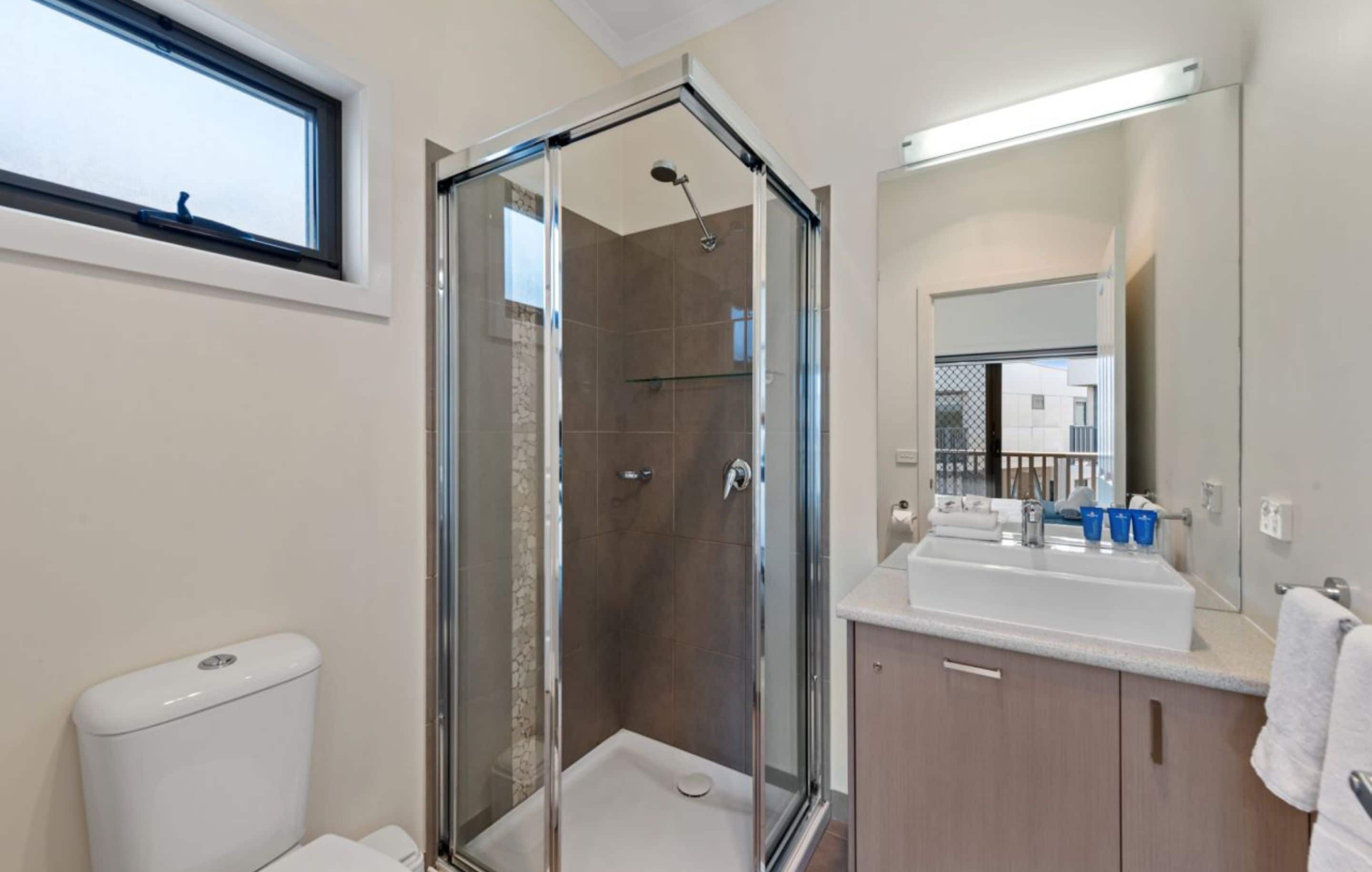 Une salle de bain moderne avec une douche à parois de verre, un lavabo blanc et un grand miroir.
