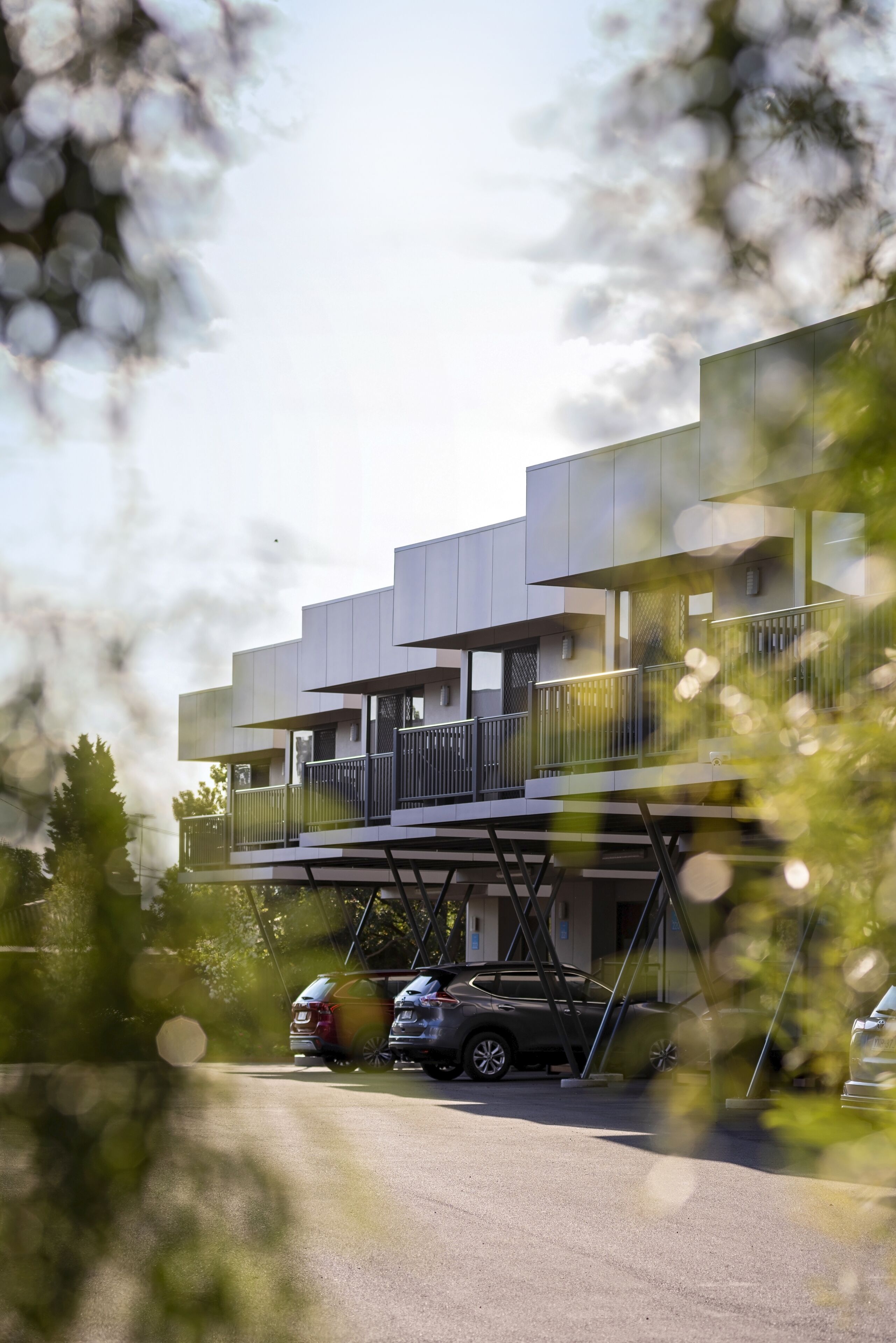 A modern building with multiple levels, a covered parking area, and a few cars parked in front.