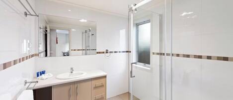 A modern bathroom with a large mirror, a sink, and a shower area.