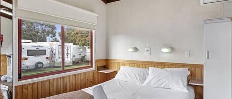 Un dormitorio con una cama grande, una ventana que da a vehículos recreativos, paredes de madera y un armario blanco.
