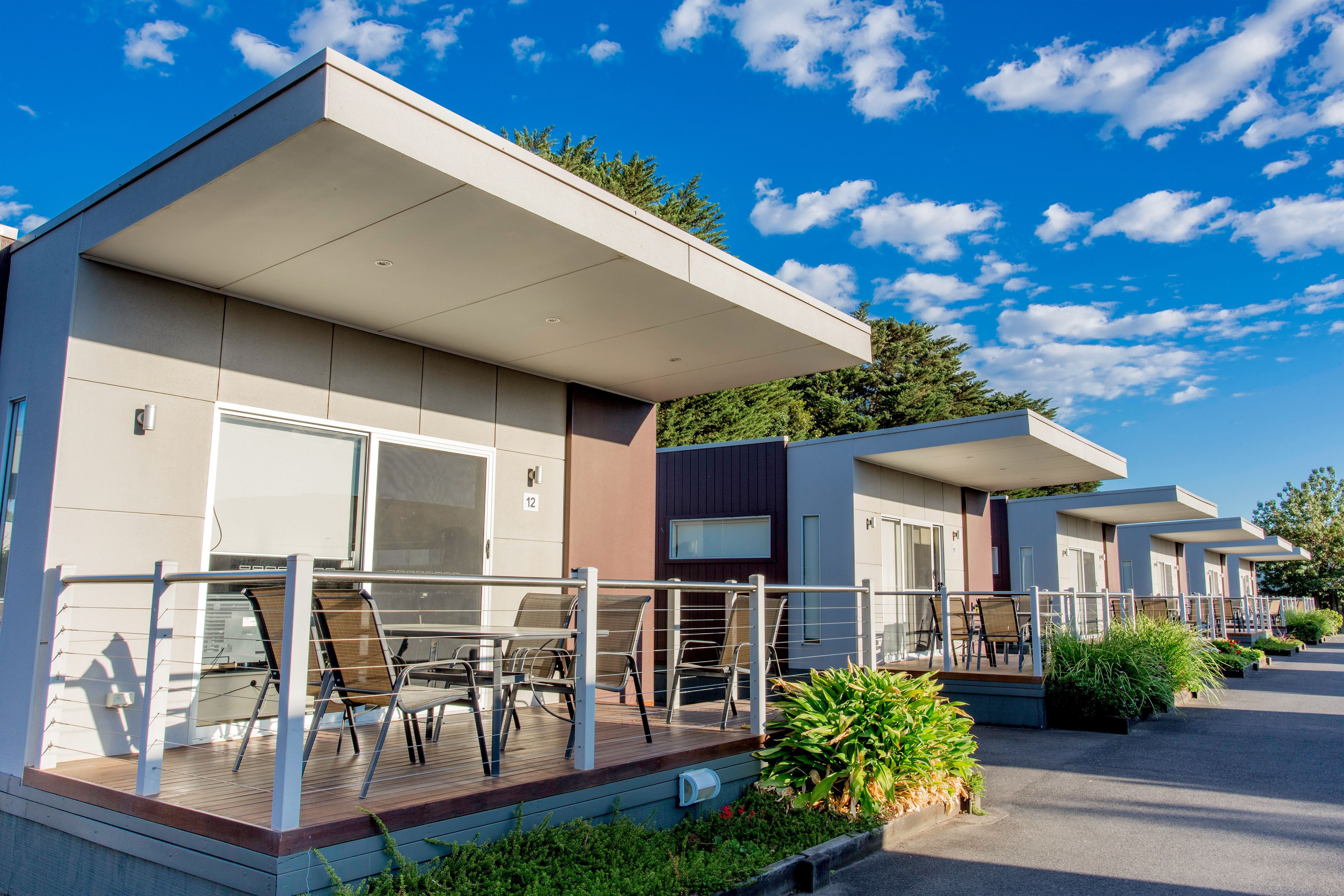 A row of modern, single-story cabins with outdoor seating areas and a covered porch.