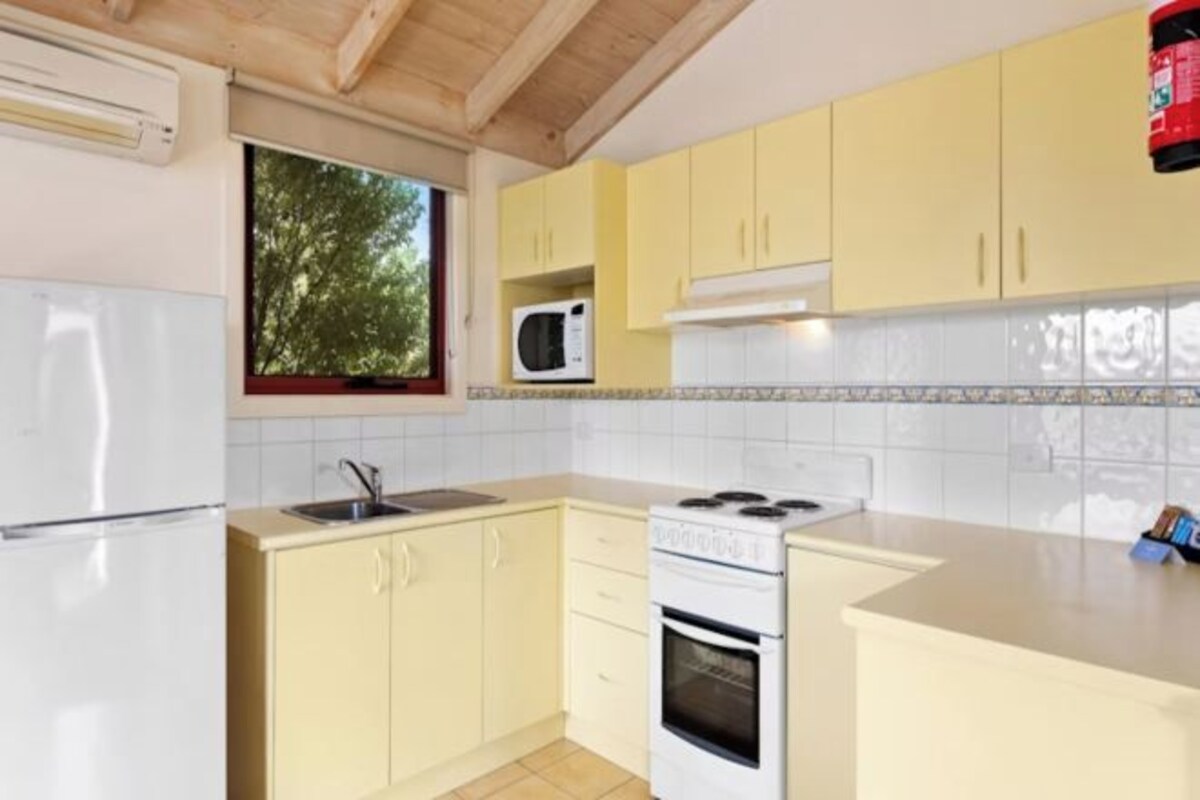 Une cuisine avec des meubles de couleur jaune, un fourneau blanc, un four à micro-ondes et une fenêtre donnant sur des arbres.