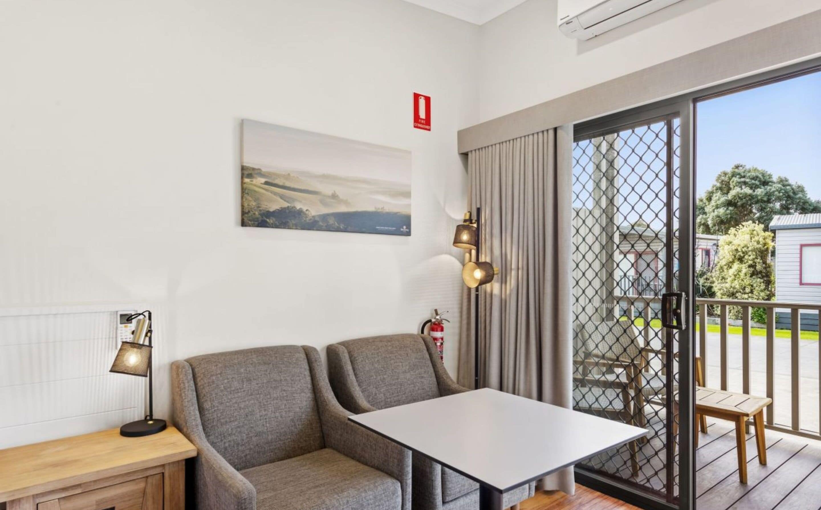 Una habitación moderna con un sofá gris, una mesita, una lámpara y un cuadro en la pared.