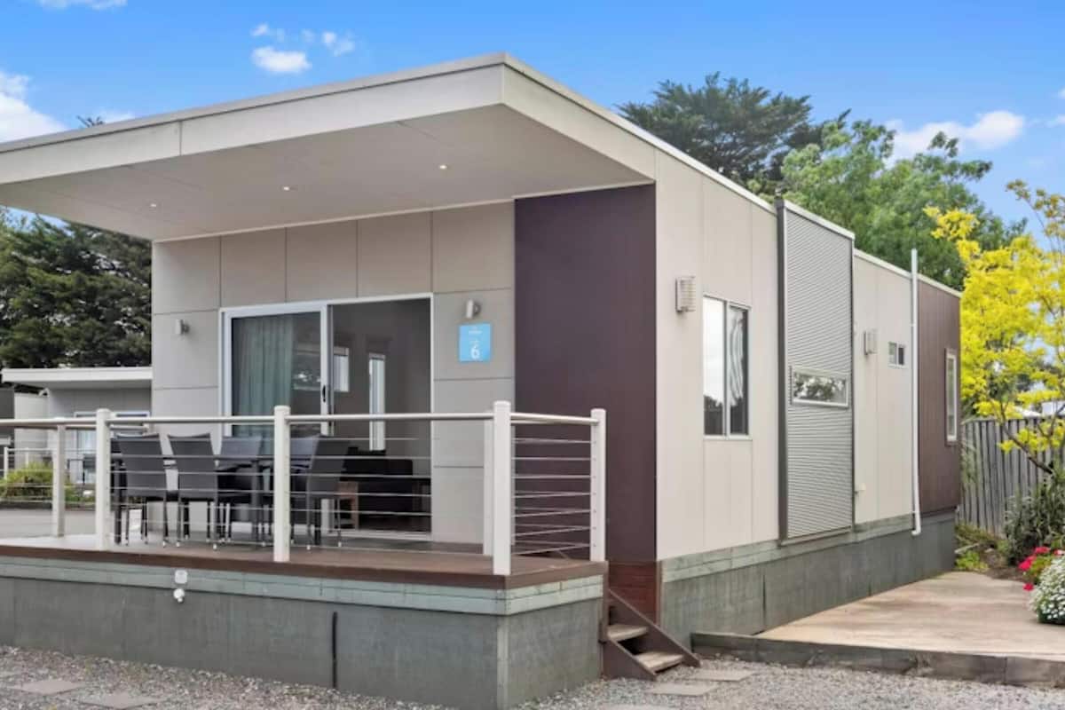 Un edificio moderno con un área de asientos cubierta al aire libre, una escalera que conduce a un nivel superior y un jardín cercado.