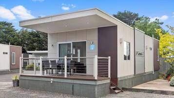 A modern building with a covered outdoor seating area, a staircase leading to an upper level, and a fenced garden area.