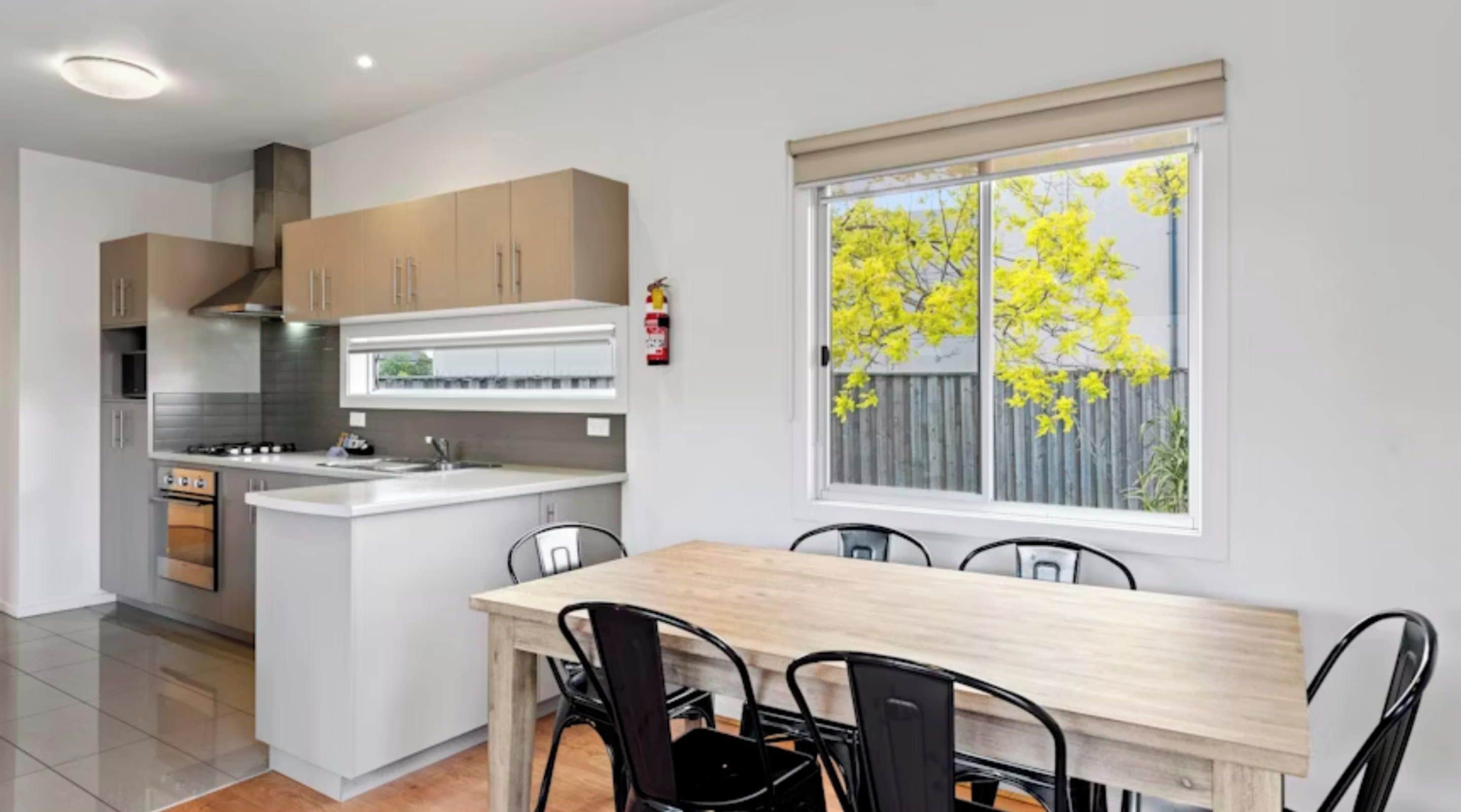 A modern kitchen with a central island, wooden cabinets, and a dining area with a table and chairs.