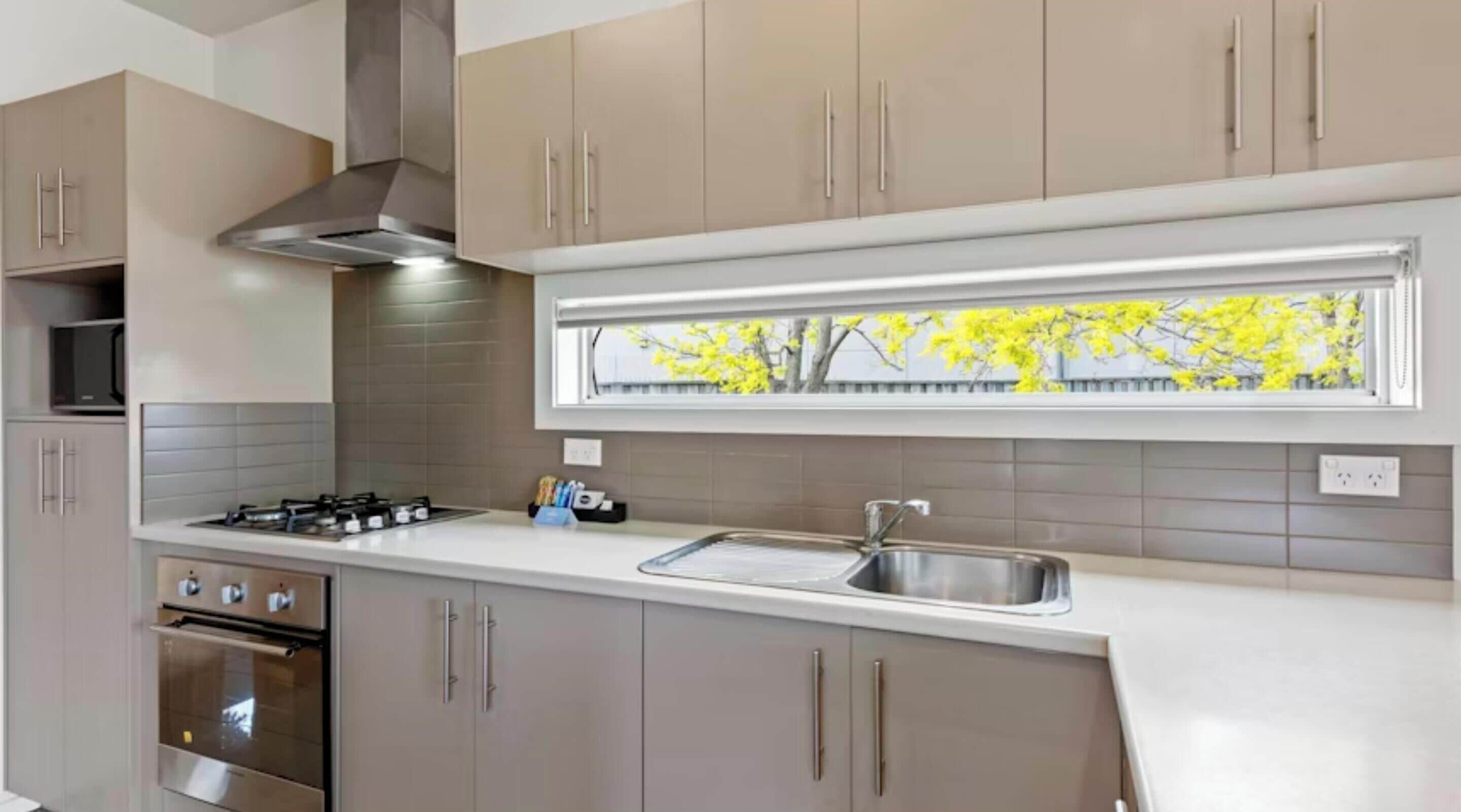 A modern kitchen with stainless steel appliances, a window with a view of yellow trees, and light-colored cabinetry.