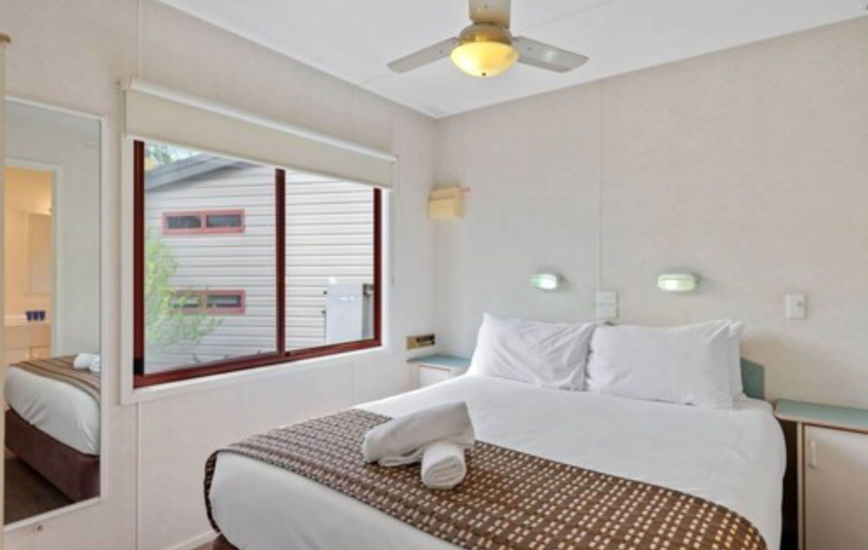A hotel room with a bed, a window, a ceiling fan, and a nightstand.