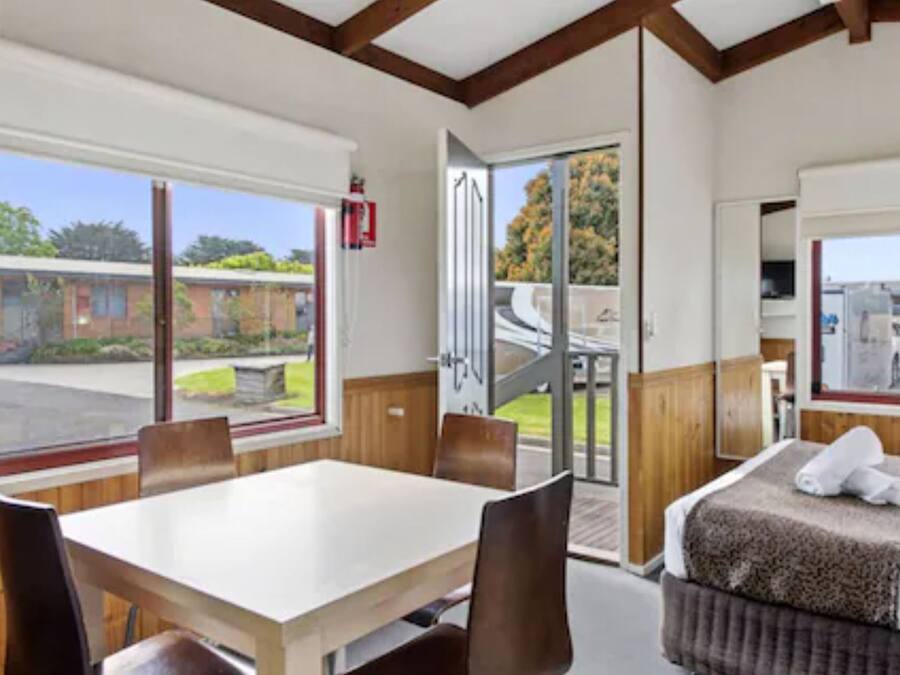 Habitación de hotel con una cama, una mesa y sillas. Se ve una ventana con vistas al exterior.