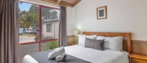 Una habitación de hotel con una cama grande, cabecera de madera, una mesita de noche, una lámpara y una ventana con cortinas.