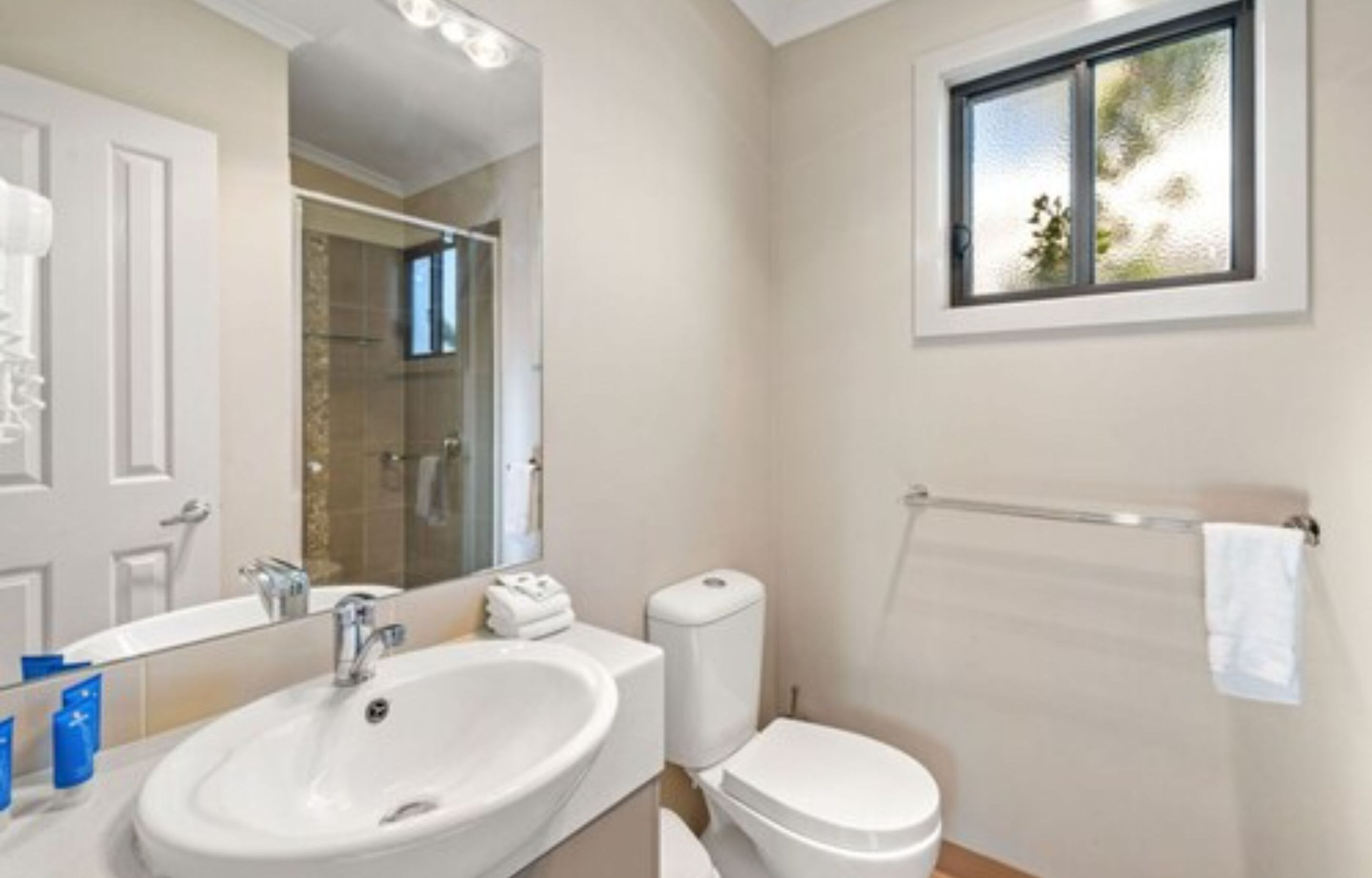 A modern bathroom with a large sink, toilet, and a window with a view.