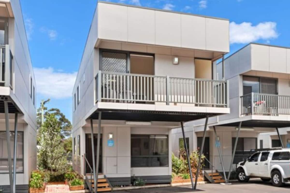 Un edificio residencial moderno de varios pisos con balcones, un garaje cubierto y un pequeño jardín.