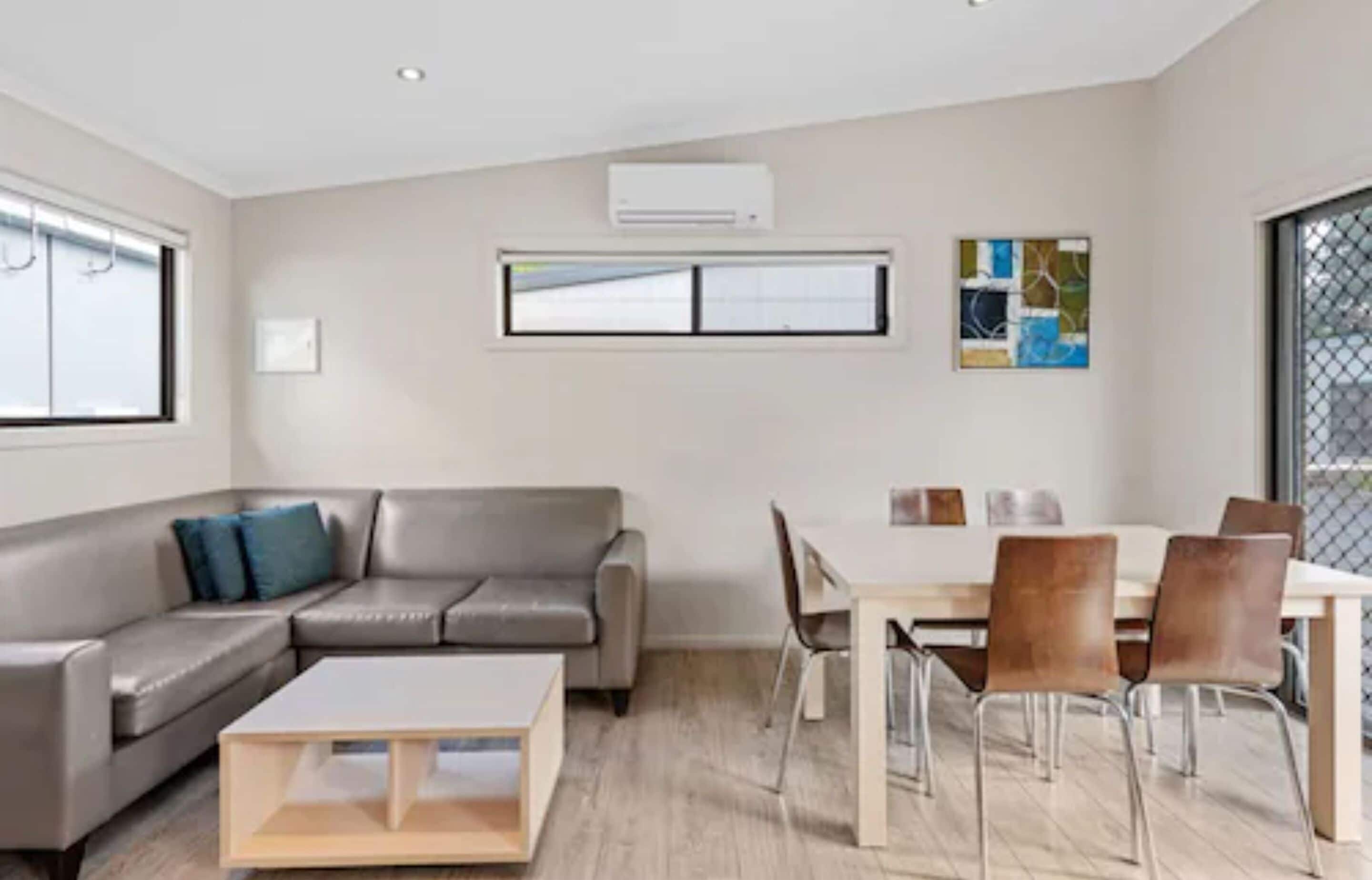 Una sala moderna con sofá, mesa de centro, mesa de comedor con sillas y una obra de arte en la pared.