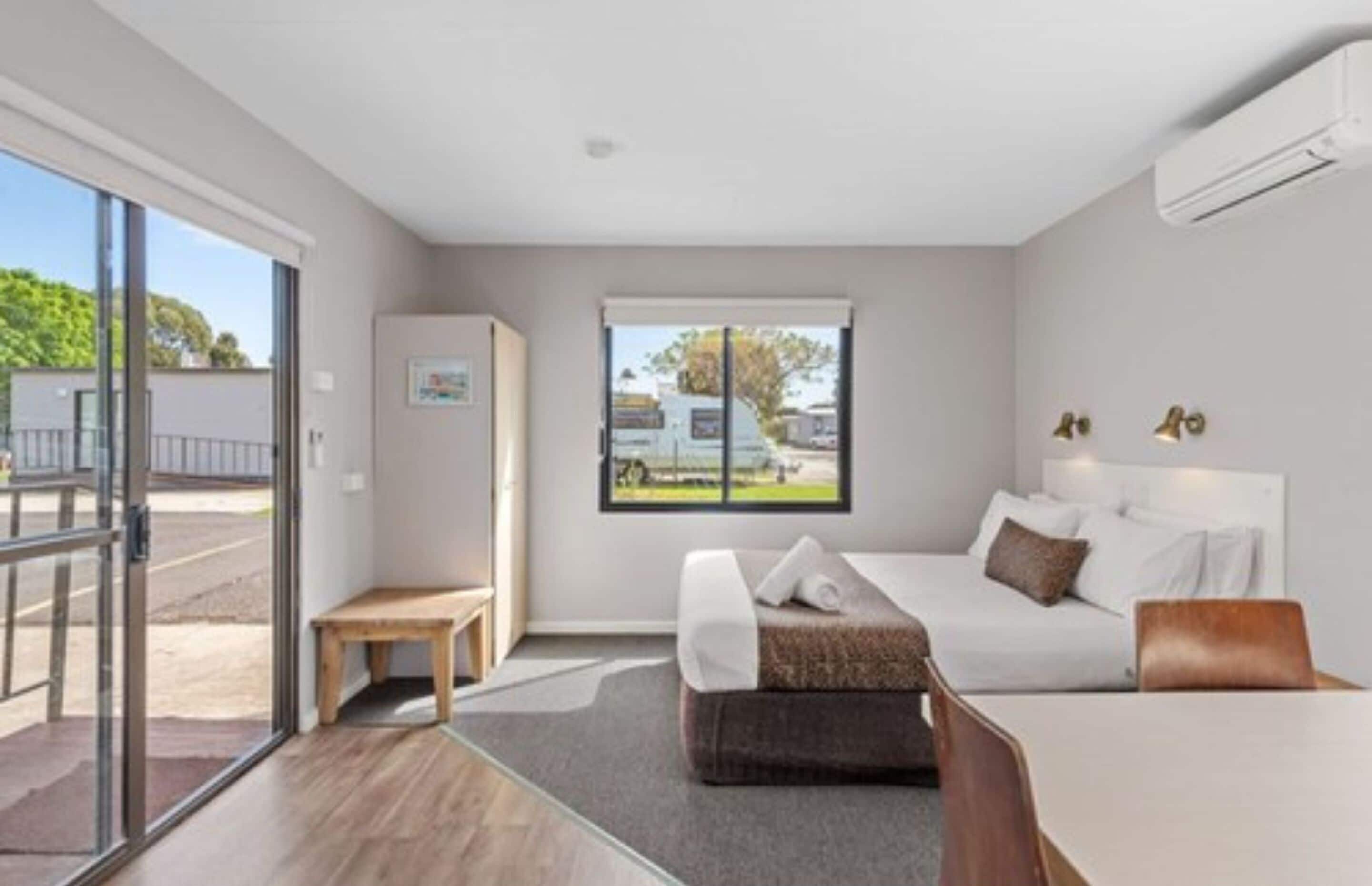 A modern hotel room with a bed, a desk, and a window with a view of the outside.