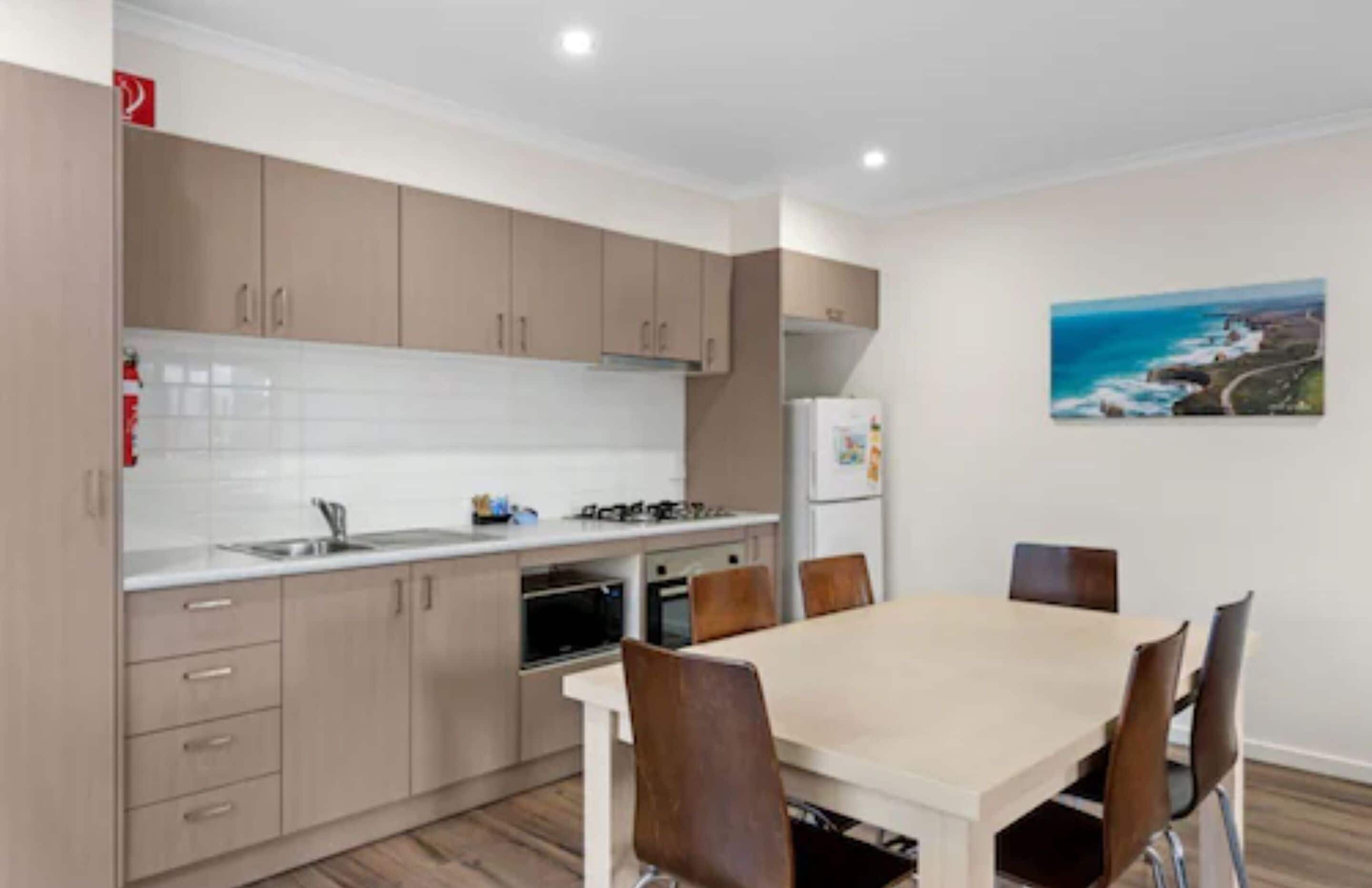 Een moderne keuken met beige kastjes, een wit aanrechtblad en een eethoek met een tafel en stoelen.