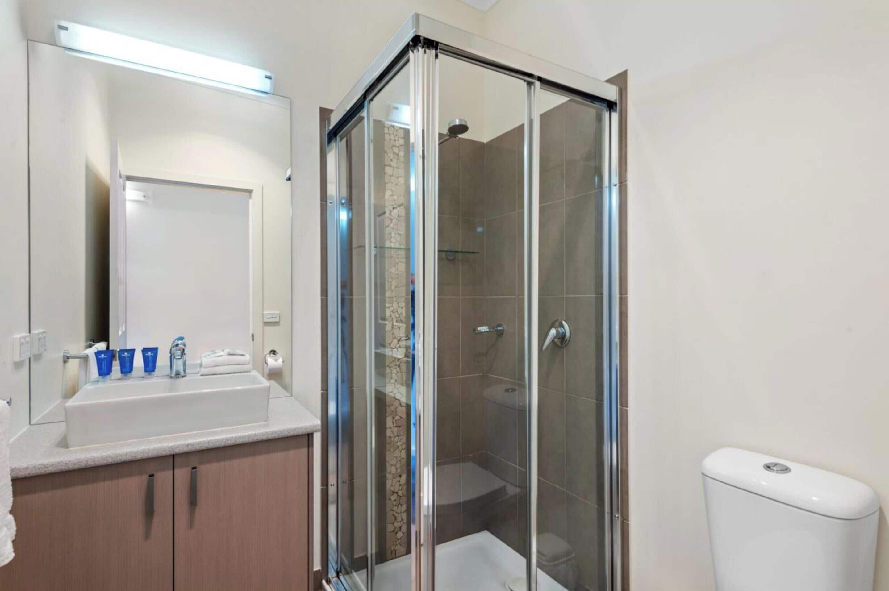 A modern bathroom with a glass-enclosed shower, a white sink with blue cups, and a toilet.