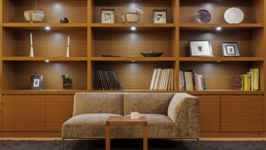 A living room with a sofa, a coffee table, and a wooden bookshelf with various items. - Candeo Hotels Uenokoen (Tokyo)