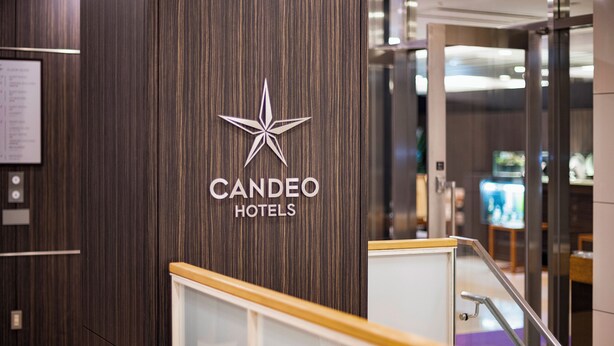 A hotel entrance with a wooden panel design and a star logo. - Candeo Hotels Uenokoen (Tokyo)
