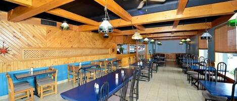 Un restaurante con vigas de madera, mesas azules y lámparas colgantes.
