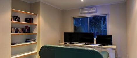 A room with a desk, two monitors, a bookshelf, and a green couch.