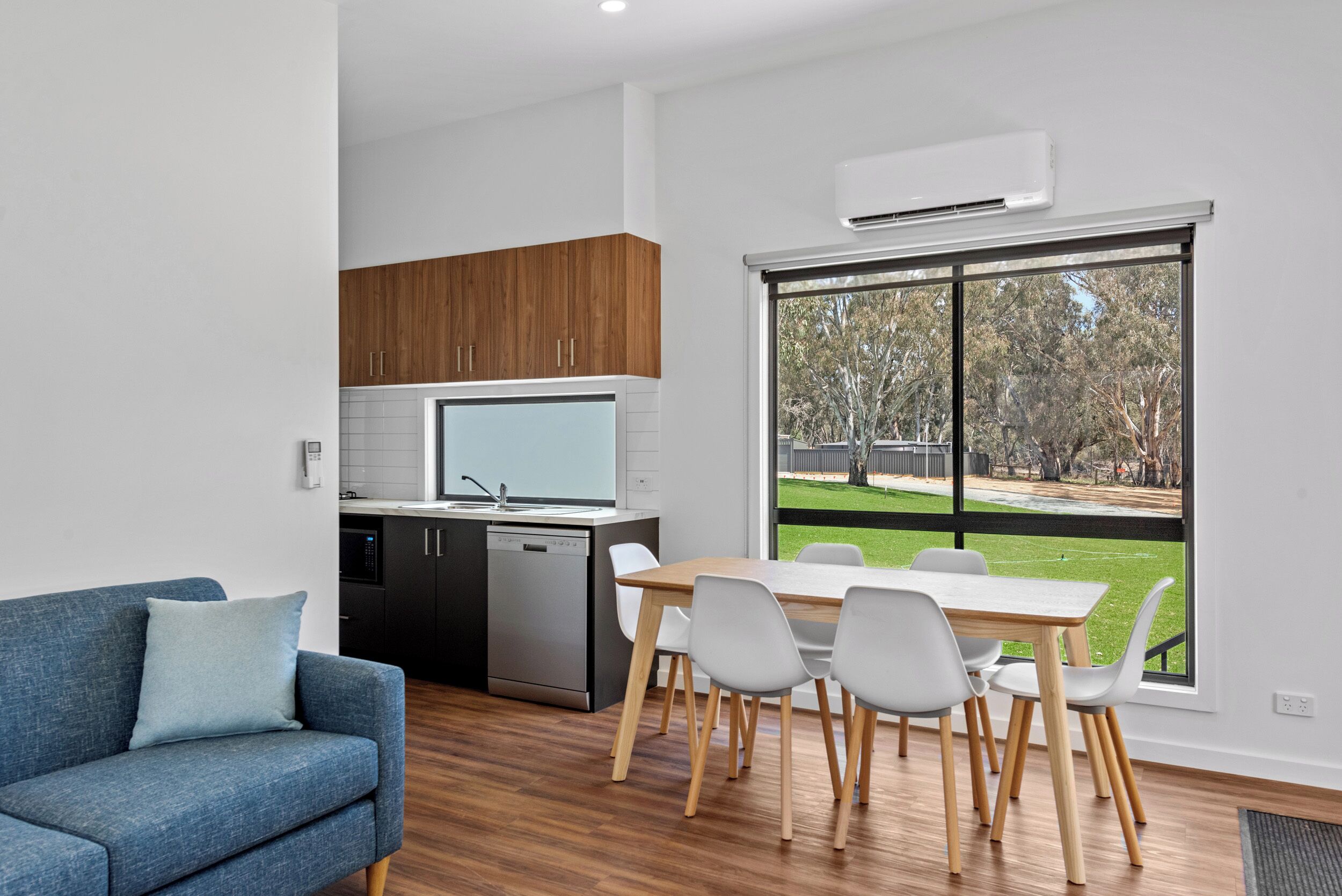 A modern kitchen with wooden cabinets, a dishwasher, and a large window offering a view of a grassy area.