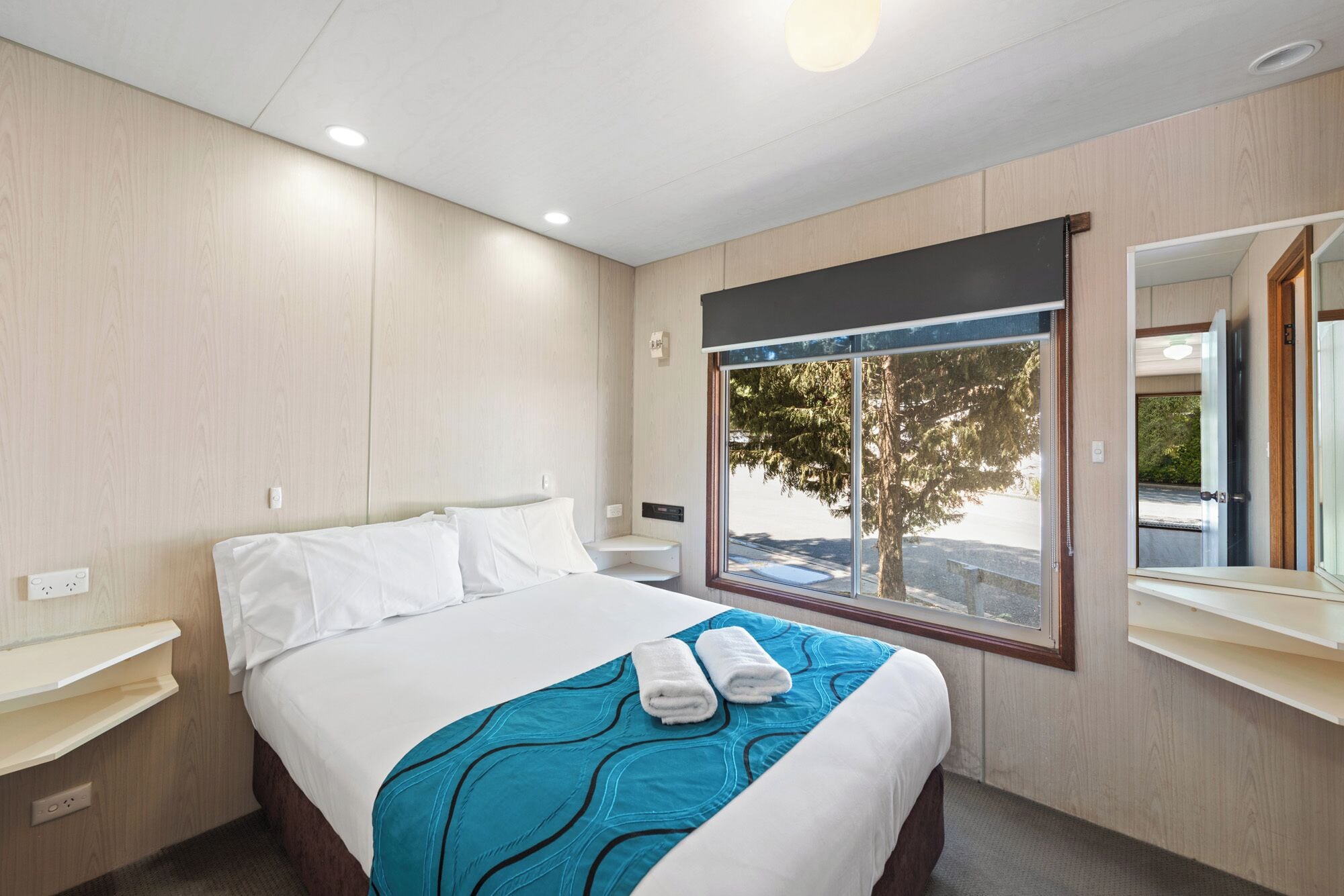 Une chambre d’h ôtel avec un lit, une fenêtre donnant sur des arbres, un miroir et une table de chevet.