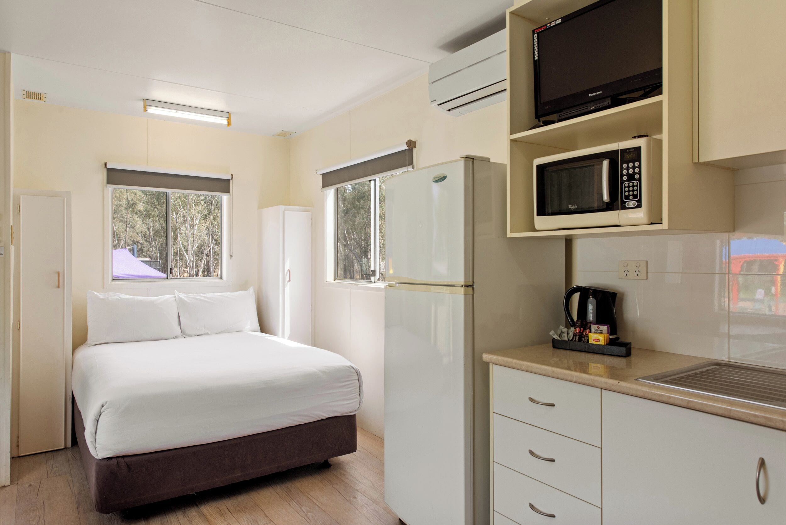 A compact hotel room with a bed, a refrigerator, a microwave, and a small kitchenette.