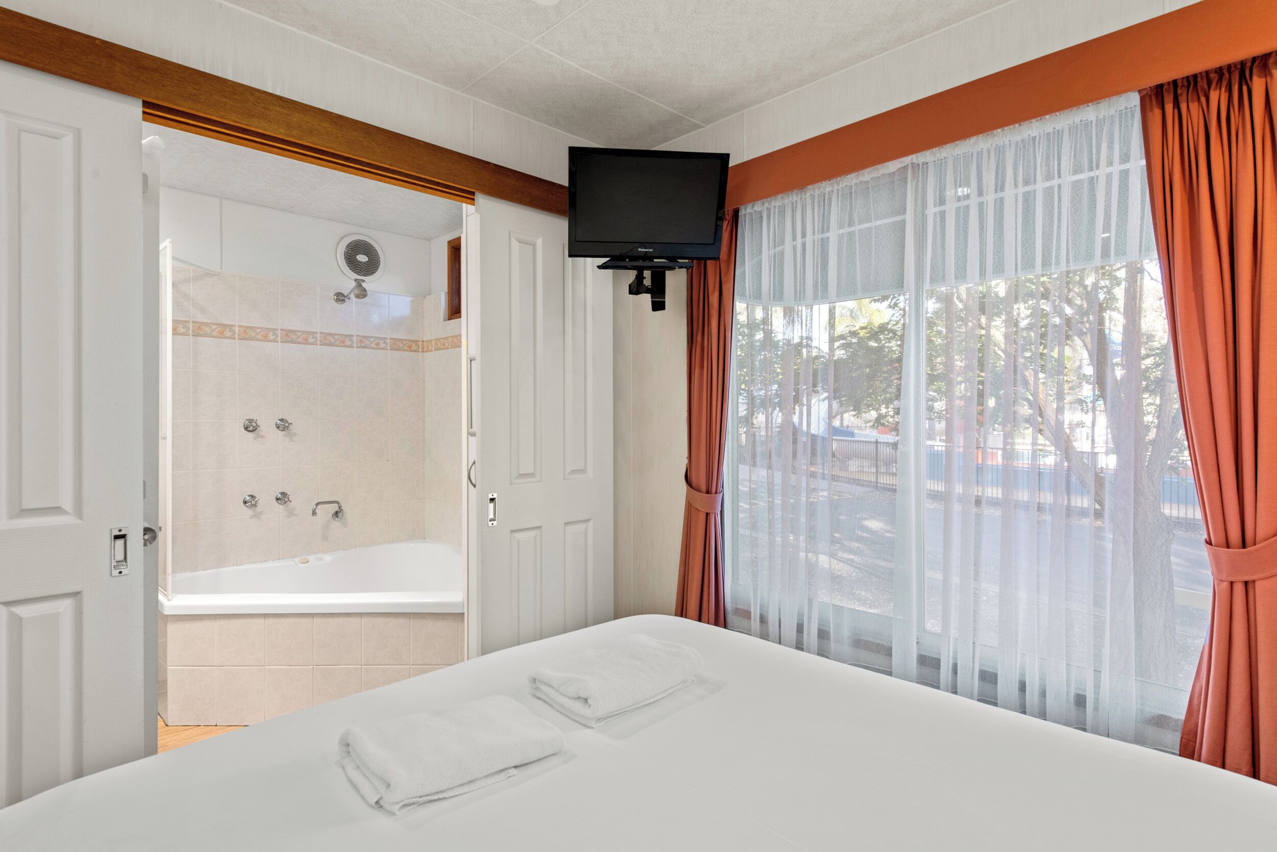 A hotel room with a large bed, a shower area, and a TV mounted on the wall.