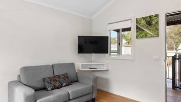 A modern living room with a grey sofa, a mounted TV, and a window with a view of greenery.
