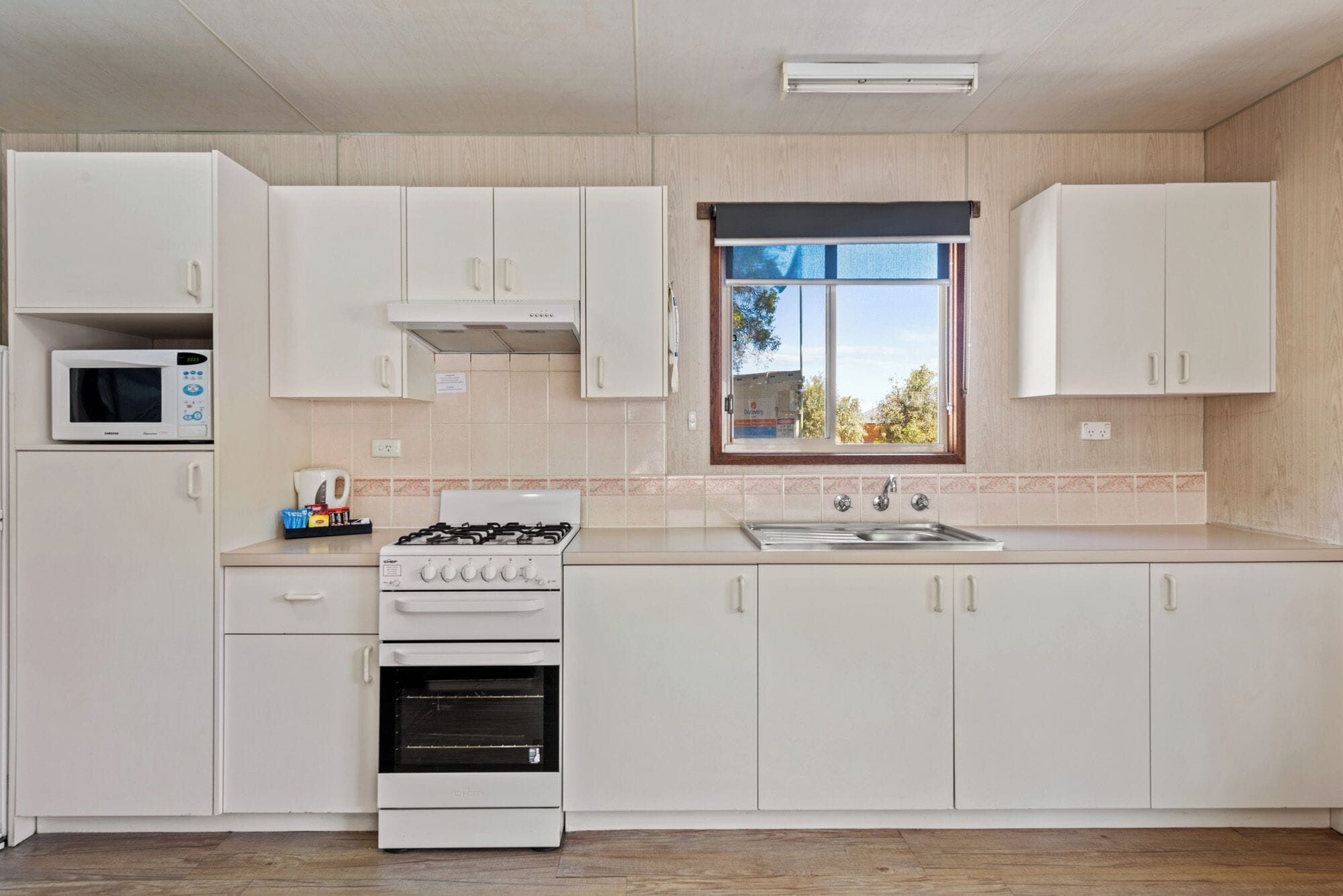 A modern kitchen with white cabinets, a built-in microwave, a gas stove, and a window with a view of trees.