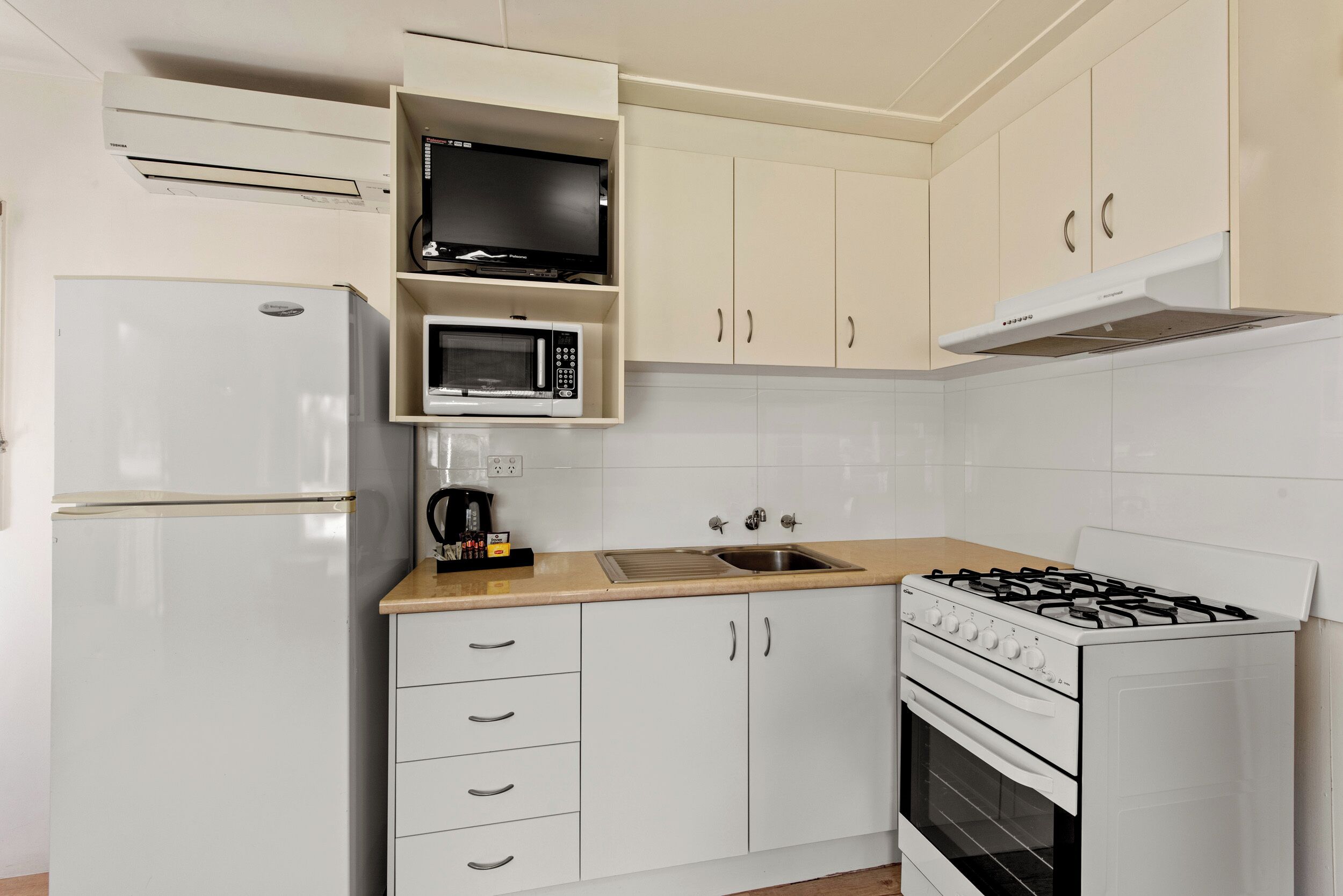 A compact kitchen with a white refrigerator, a microwave, a stove, and a sink.