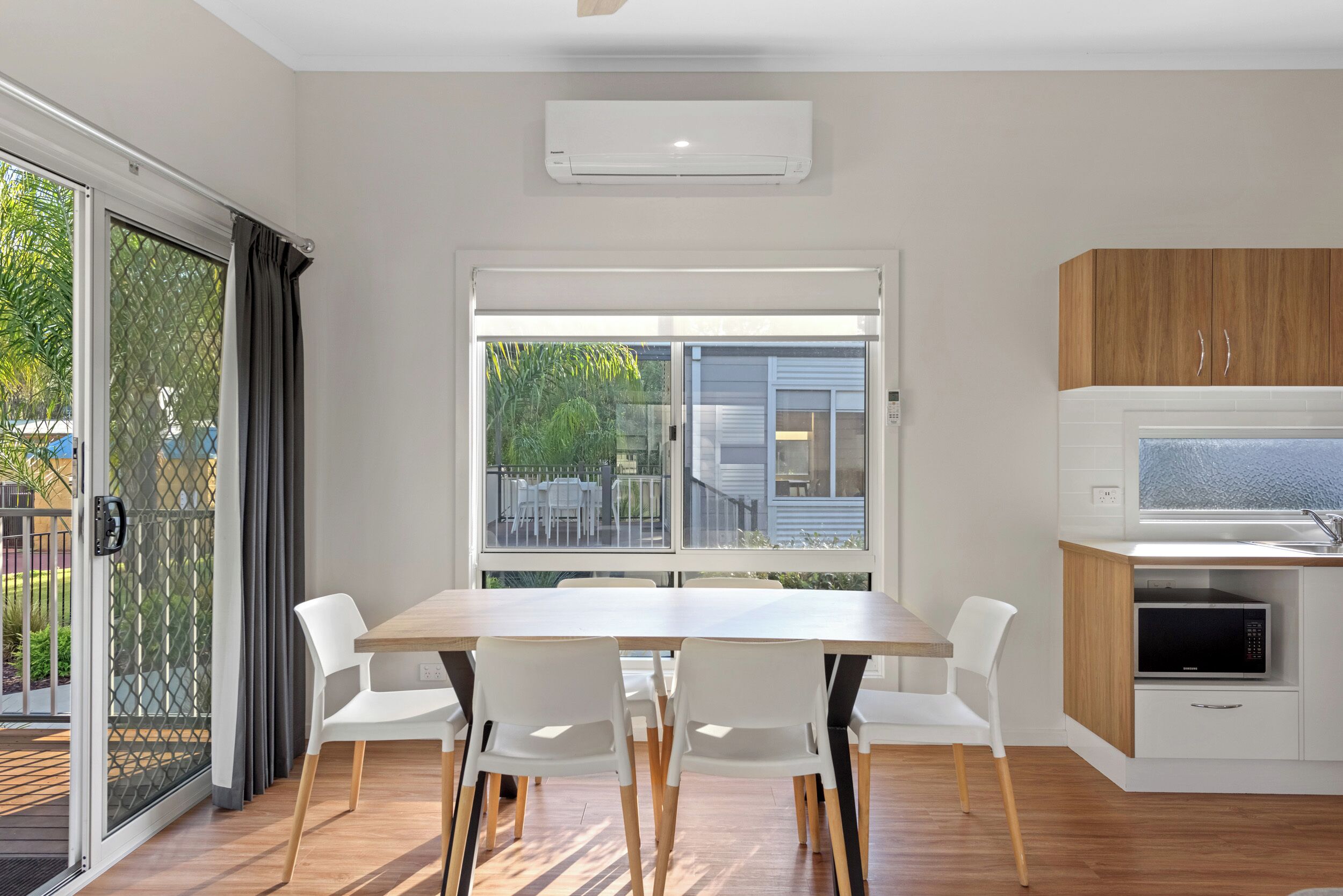 A modern kitchen with a microwave, a wooden cabinet, and a window overlooking a garden.